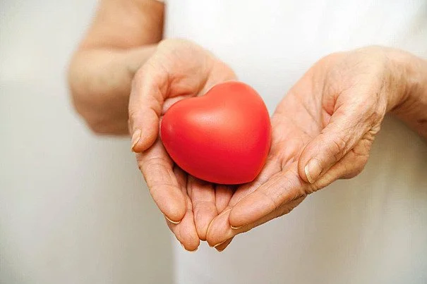Two hands holding a red heart-shaped object against a white background.