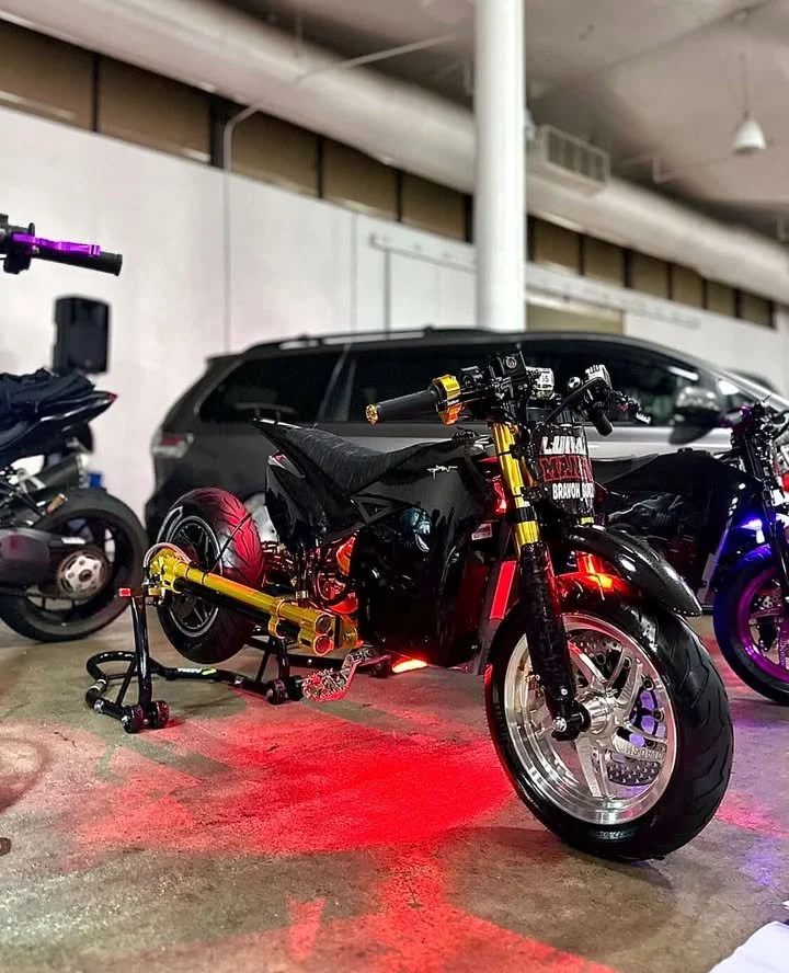 A black motorcycle with red underglow lights parked in an indoor garage, with a gray SUV and another motorcycle in the background.