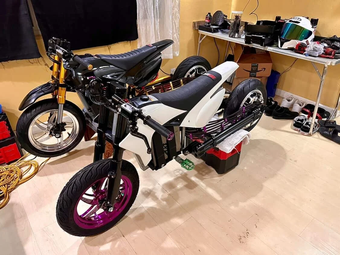 Unfinished motorcycle frame with tires in a workshop, surrounded by tools and storage boxes.