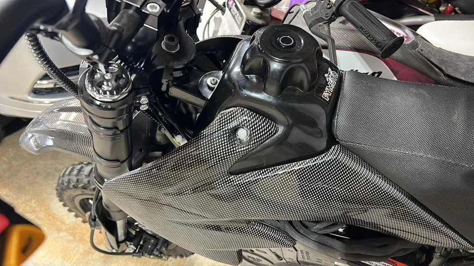 Close-up of a black motorcycle with a carbon fiber design on the tank and seat, showing the handlebars and front suspension.