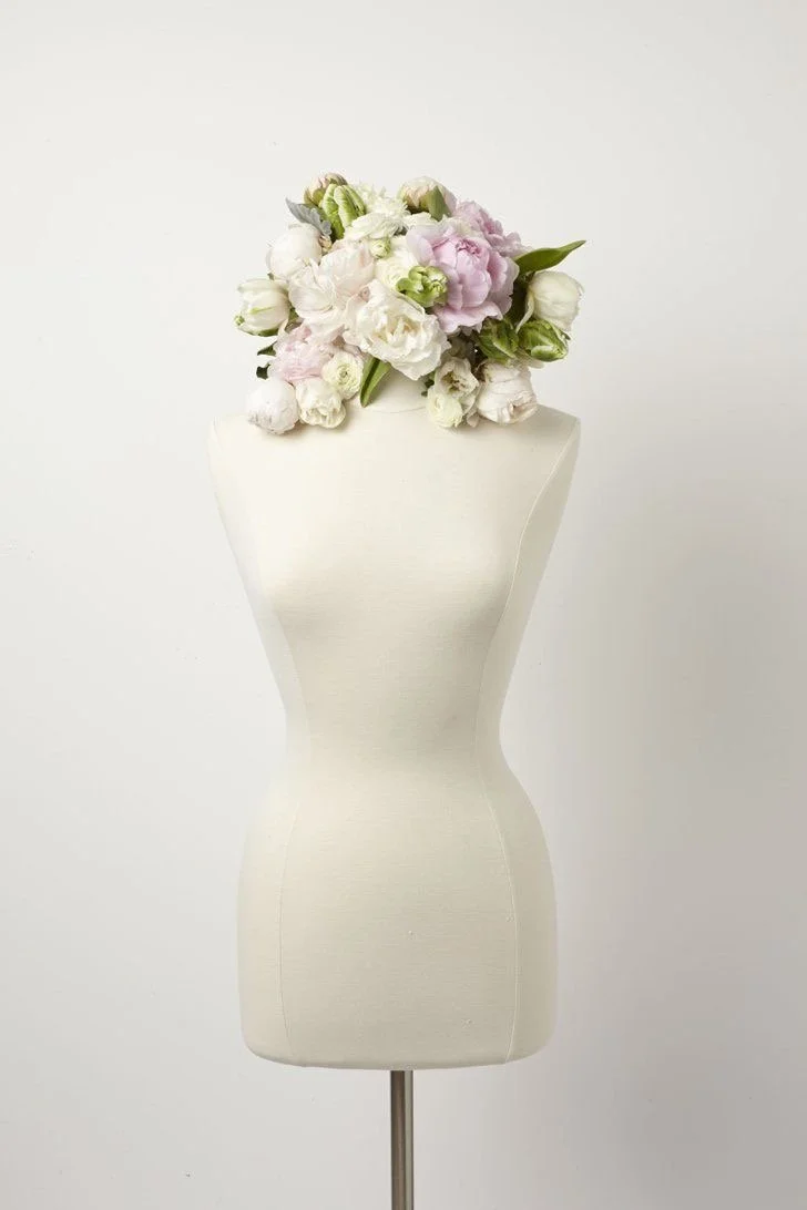 A white dress form with a bouquet of white and light pink flowers on top against a plain white background.