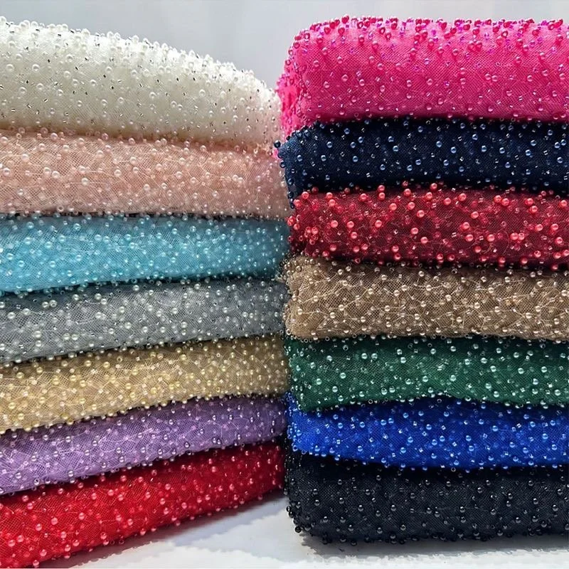 Stacks of fabric adorned with small, shiny beads in various colors including white, pink, black, red, blue, gold, purple, green, beige, and gray.