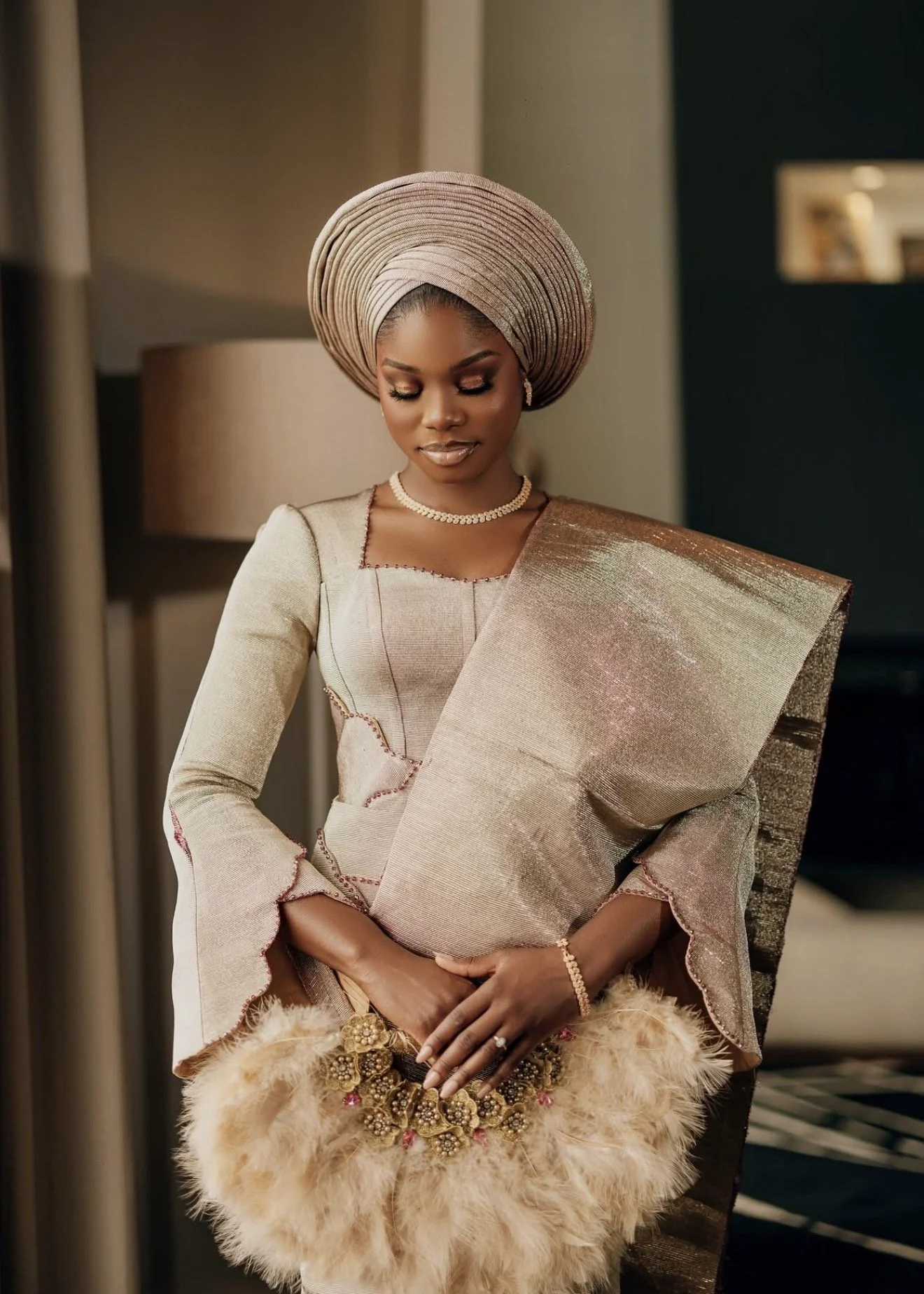 A woman and man dressed in traditional Nigerian attire, standing close together indoors near a glass railing with a city view in the background.