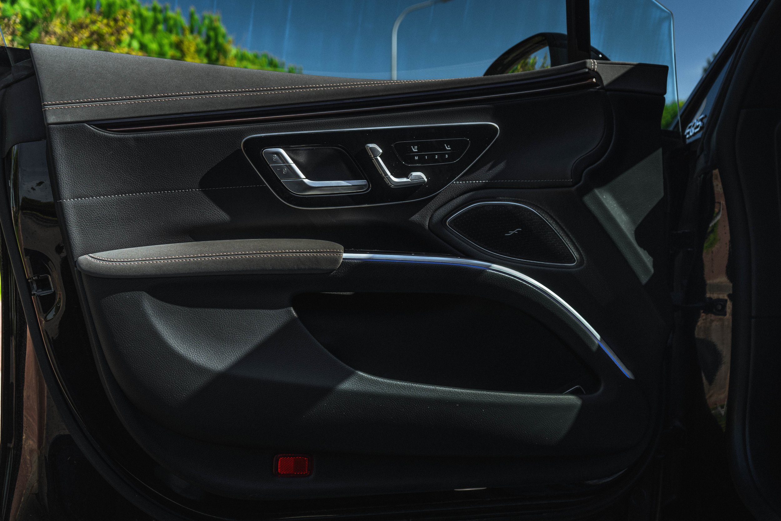 Parte interna da porta de um carro de luxo preto com detalhes de acabamento em metal e controle de ajuste de assento.