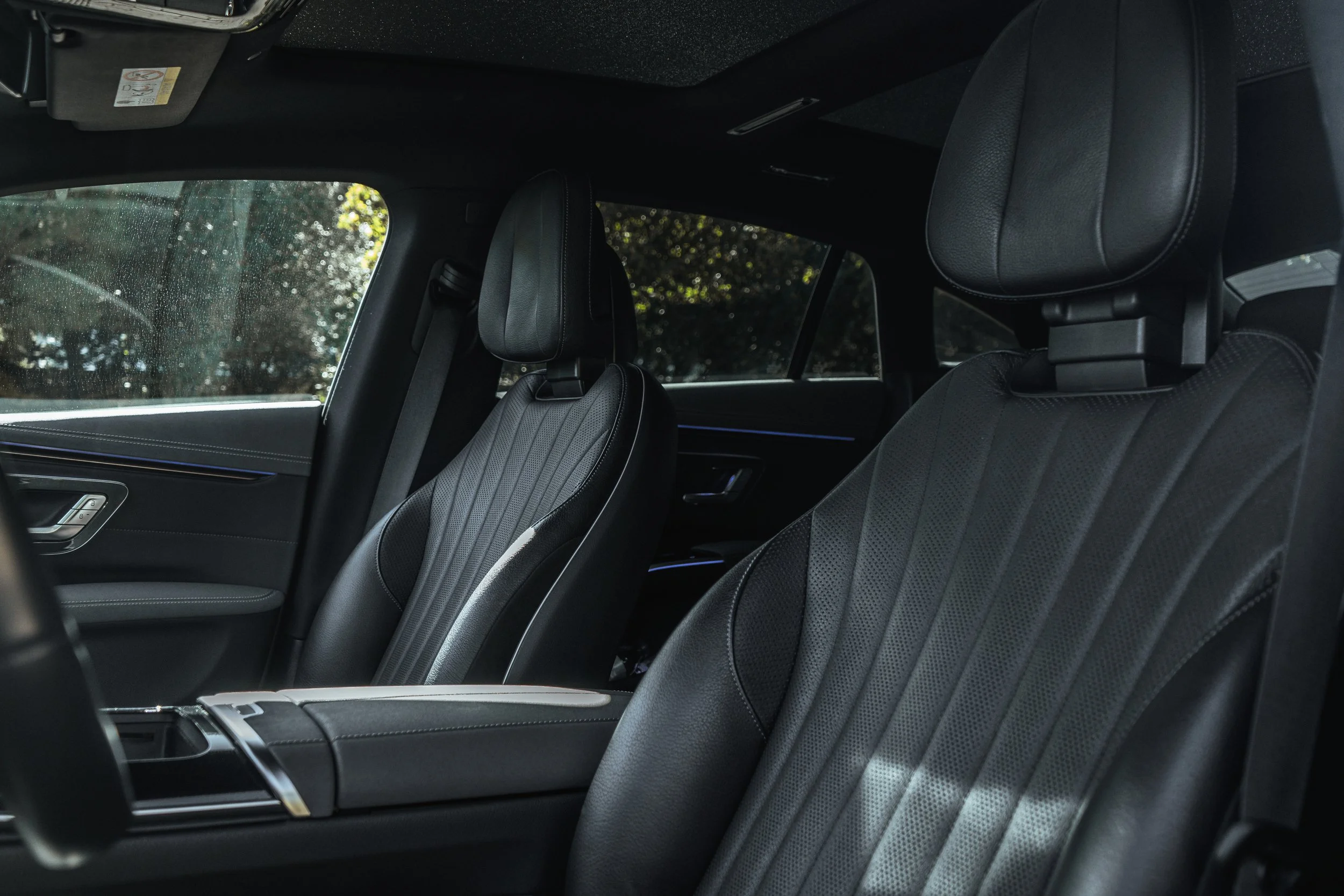 Interior de um carro, com assentos de couro preto, visibilidade das janelas laterais com paisagem externa.