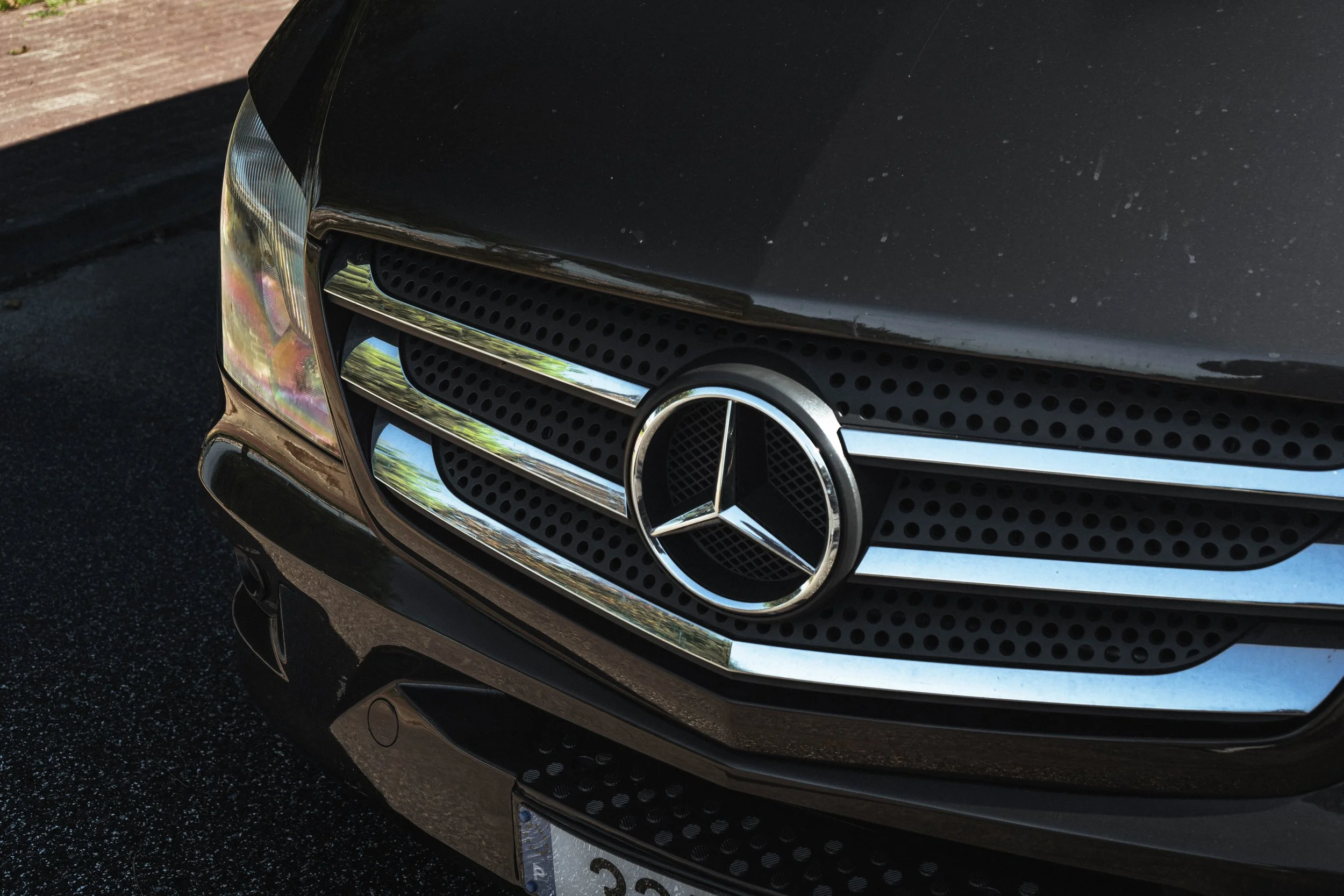 Frontal de um carro preto, Volkswagen com logo da Mercedes-Benz no centro da grade dianteira, estacionado no asfalto.