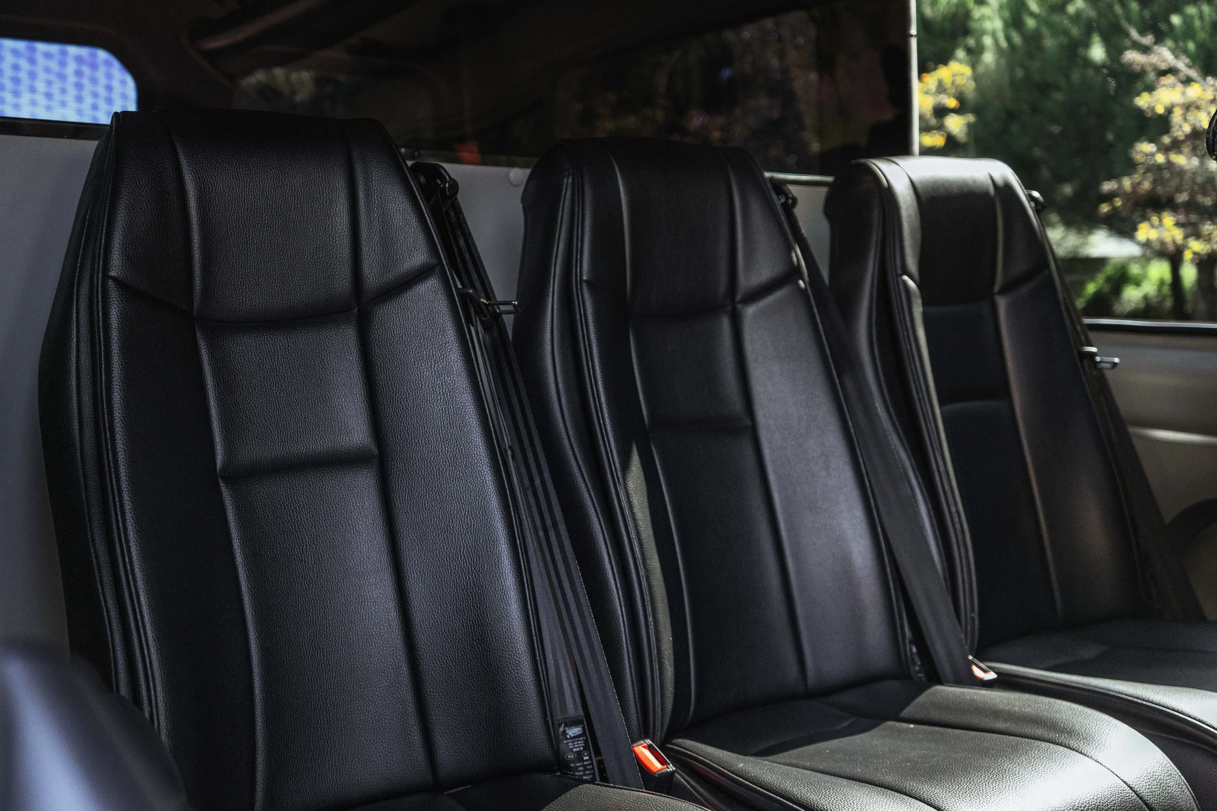 Interior de um veículo com três assentos dianteiros de couro preto.