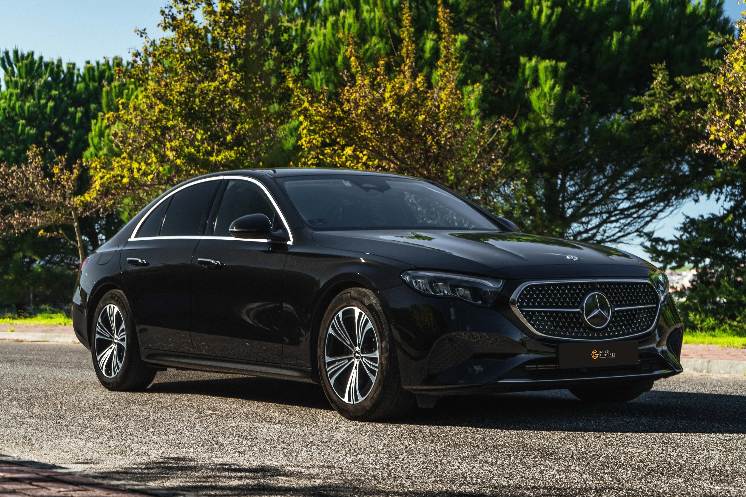 Carro preto da Mercedes-Benz estacionado na rua, com árvores verdes ao fundo.