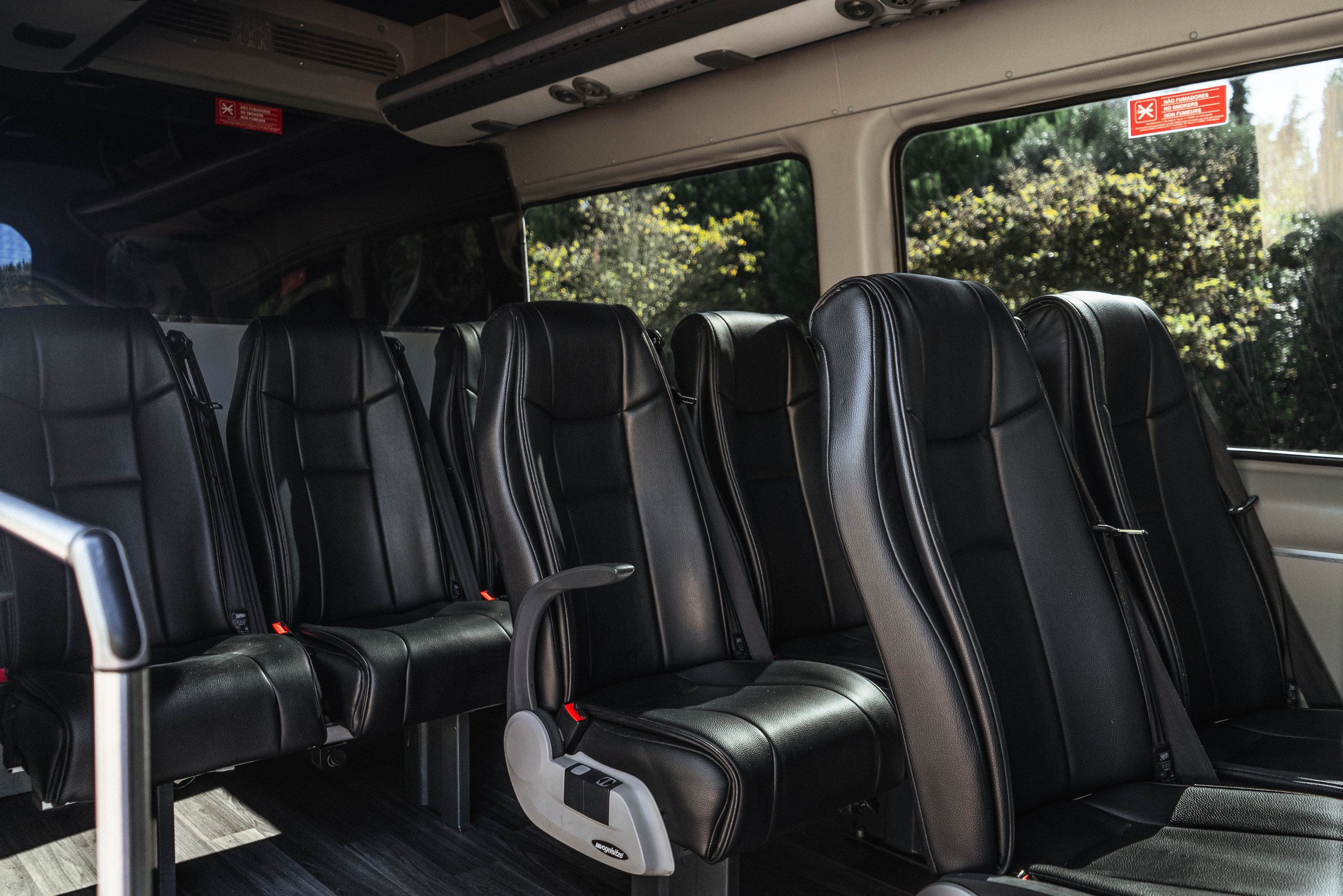 Interior de um ônibus com assentos pretos de couro e janelas que mostram árvores do lado de fora.
