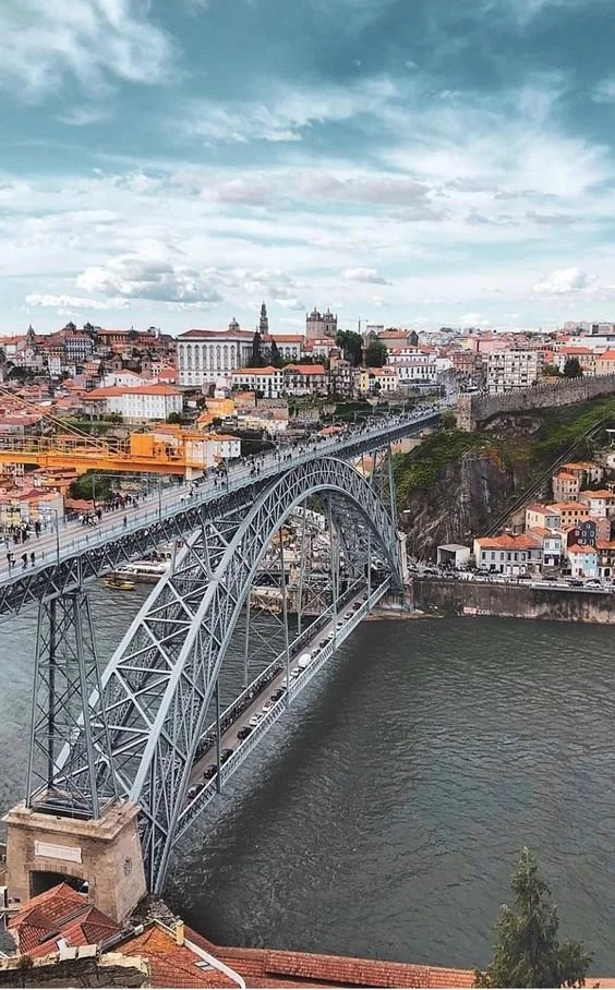 Ponte histórica de Arco de São João ligando duas margens de um rio na cidade de Porto, Portugal, com edifícios antigos ao fundo.