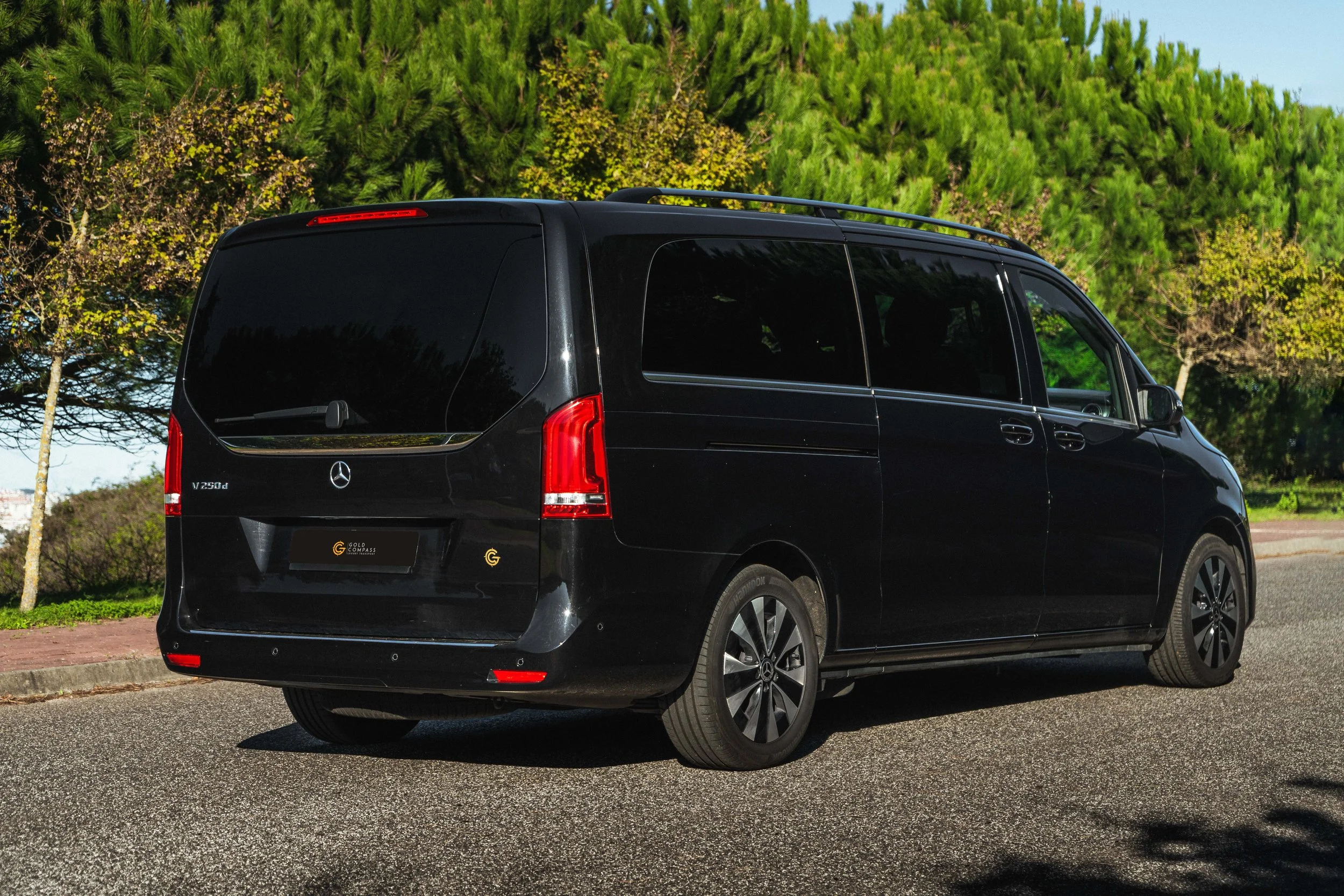 Furgoneta preta da Mercedes-Benz estacionada na rua com árvores verdes ao fundo.
