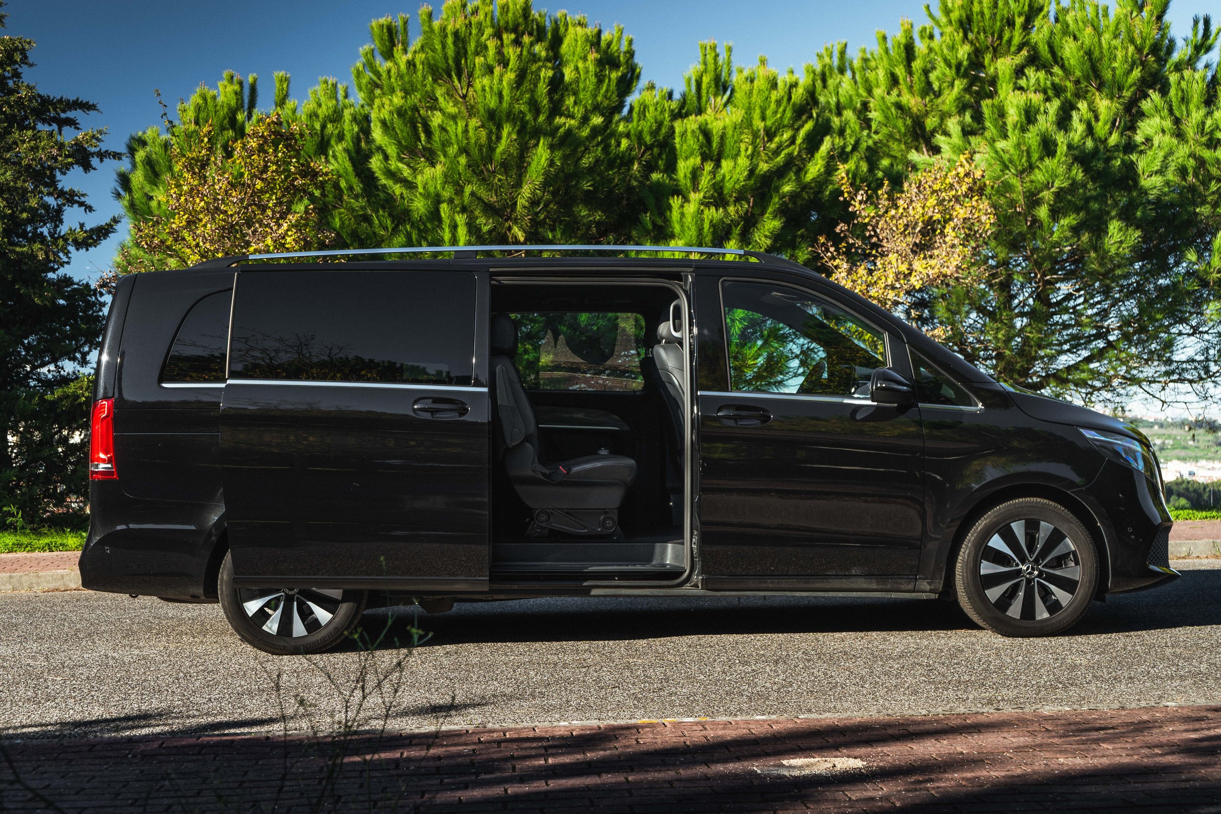 Furgão preto estacionado na rua ao lado de árvores verdes sob céu azul.