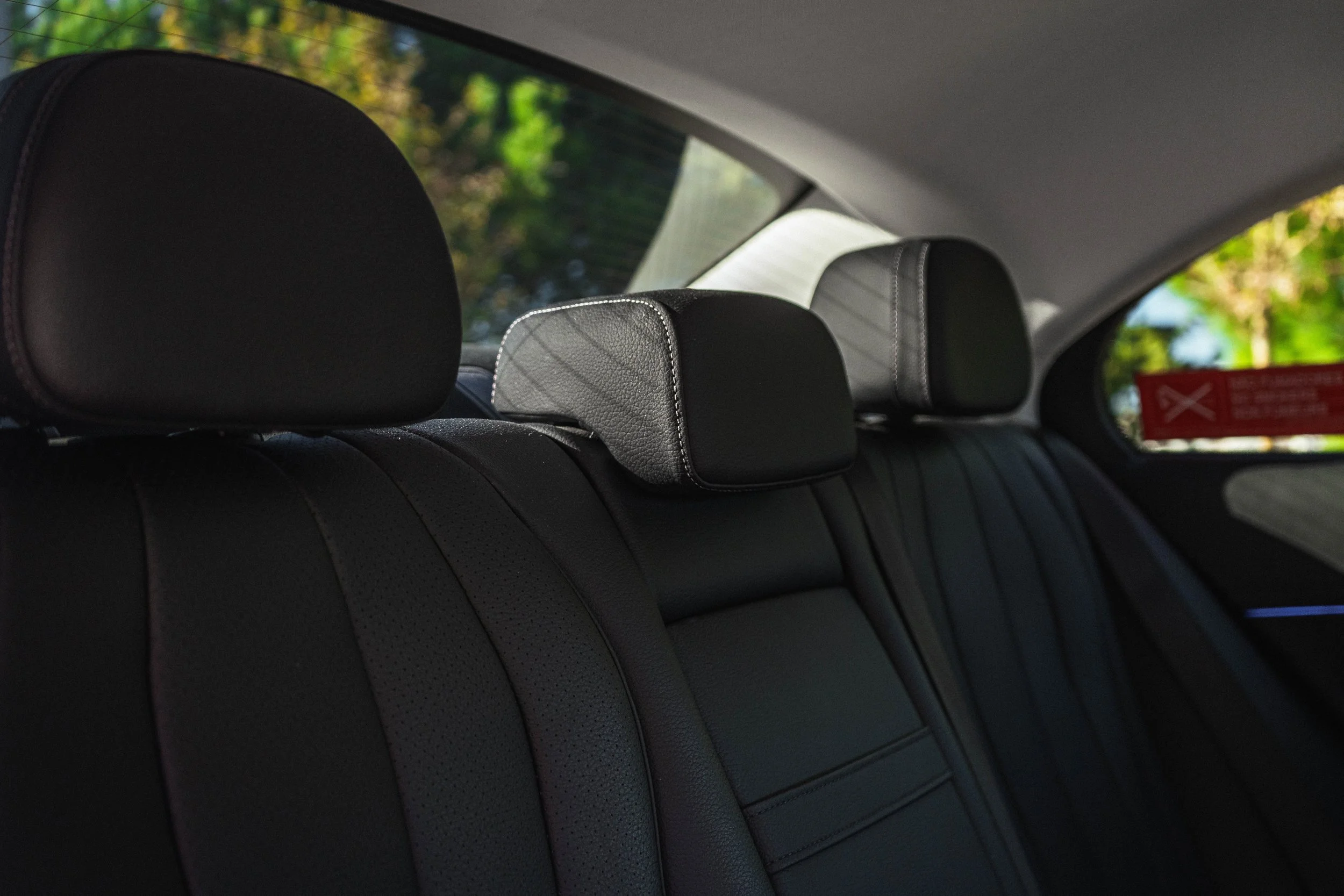 Assentos de couro preto no banco traseiro de um carro, com apoios de cabeça também de couro, vista do interior com janela ao fundo.