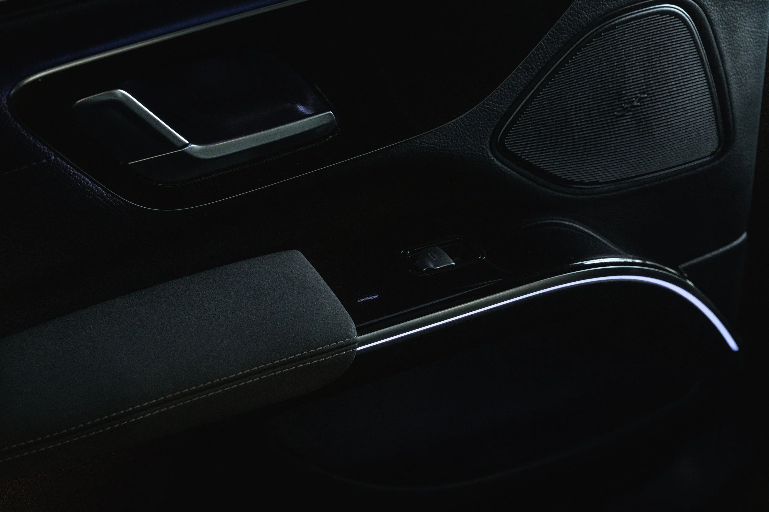 Parte interna de um carro, incluindo a maçaneta da porta, controle de janela e alto-falante, em iluminação escura.