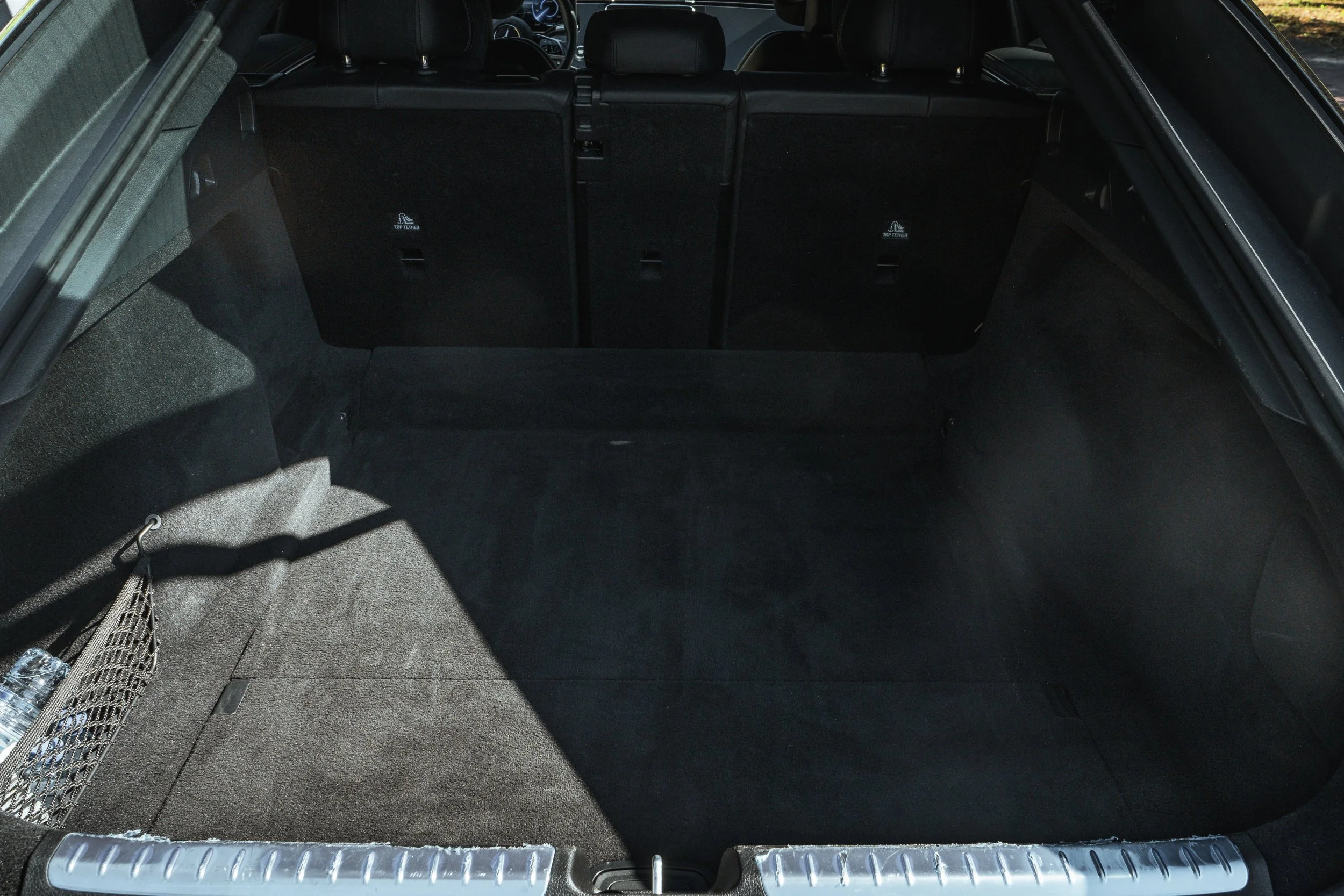 Espaço de mala de carro vazio, forrado com carpete preto, com banco traseiro dobrado e uma rede de armazenamento ao lado.