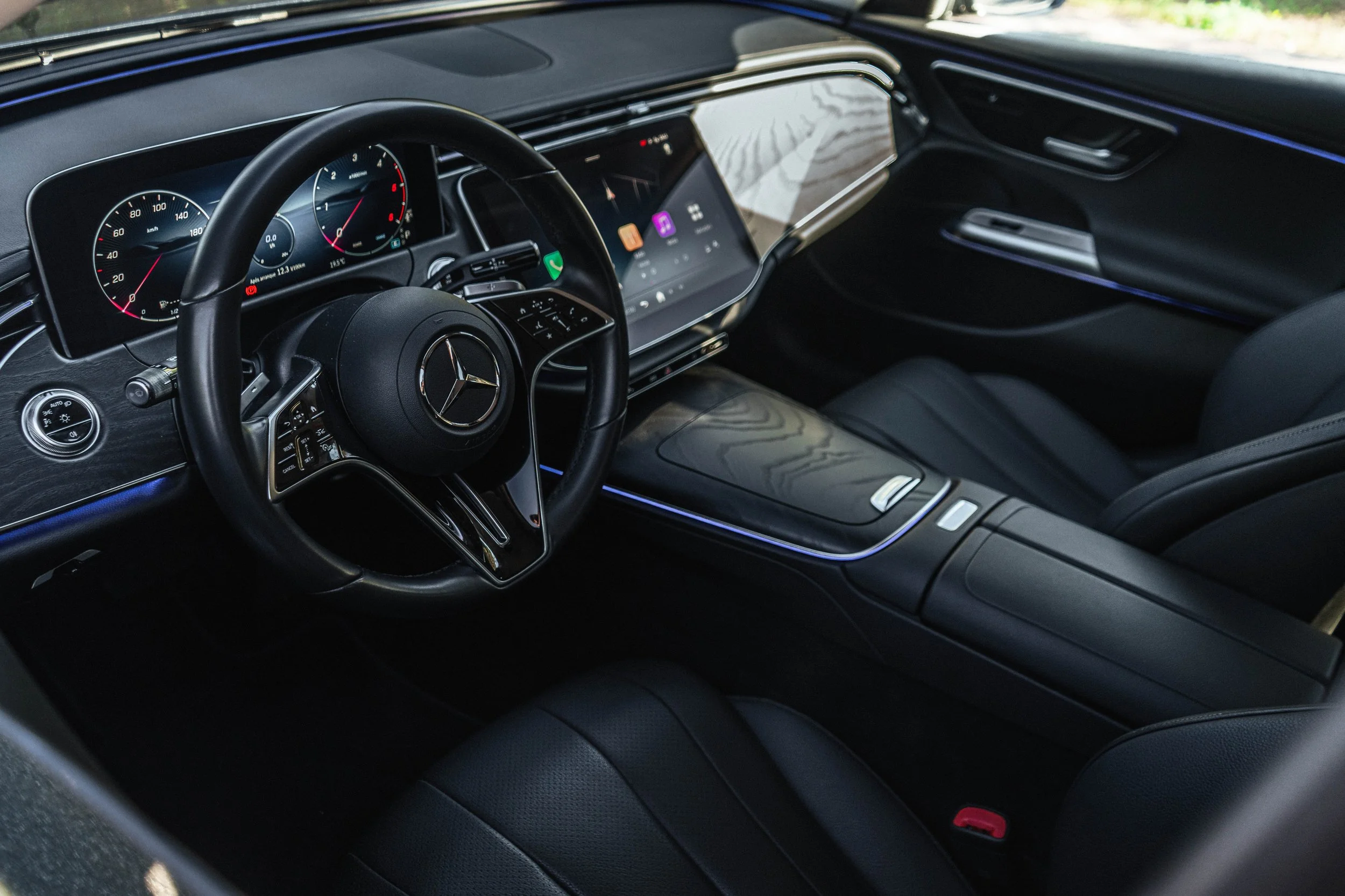 Interior de carro de luxo preto, destaque para o painel digital com velocímetro e tacômetro, volante Mercedes-Benz, sistema de infotainment no centro, assentos de couro e detalhes em iluminação ambiente.