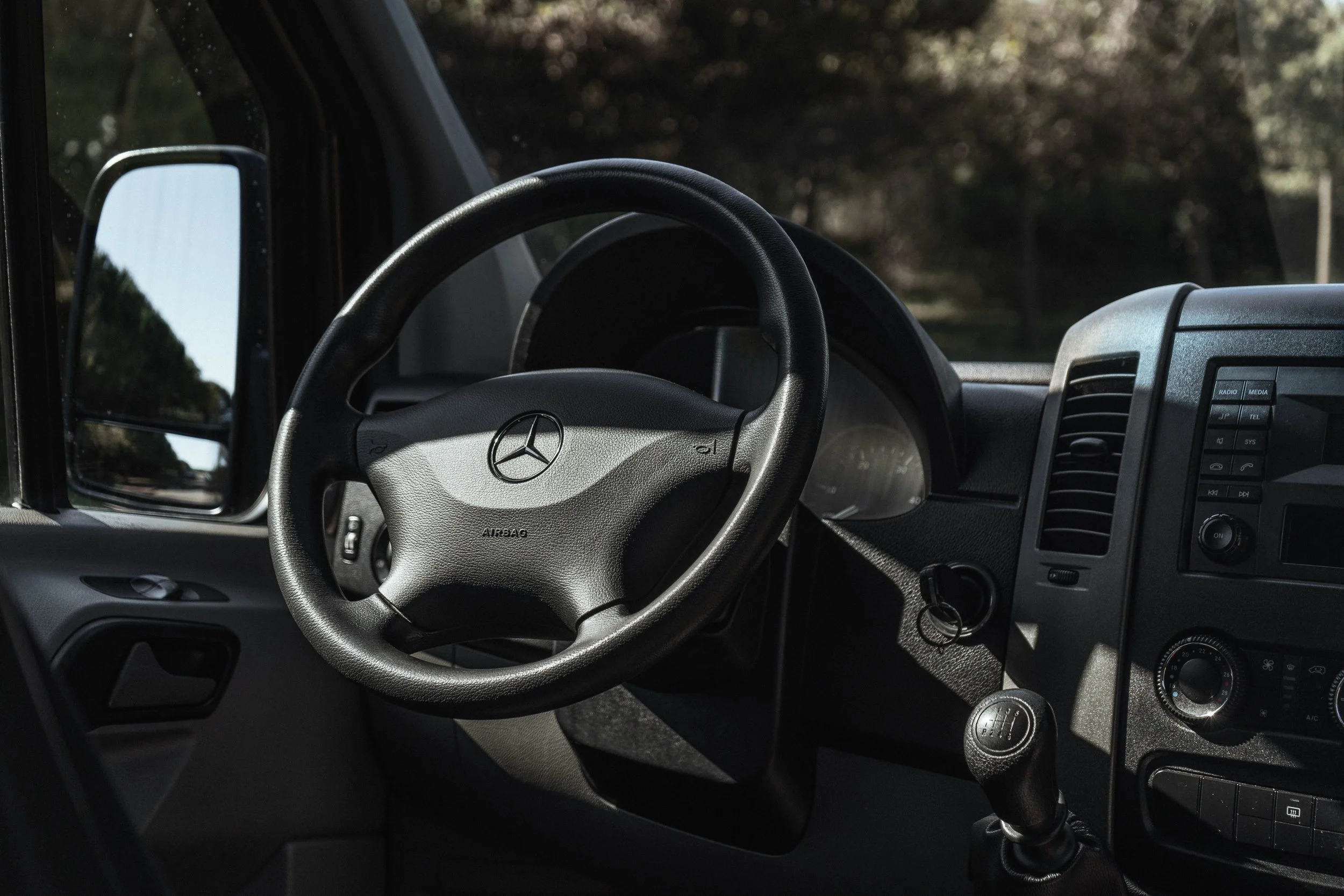 Interior de veículo, focando no volante com logo da Mercedes-Benz, painel de instrumentos, controle de clima e painel de áudio.