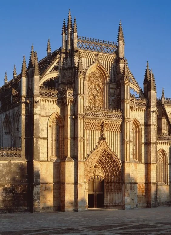 Fachada de uma catedral gótica com detalhes arquitetônicos elaborados, portões altos e torres pontiagudas ao nascer do sol.