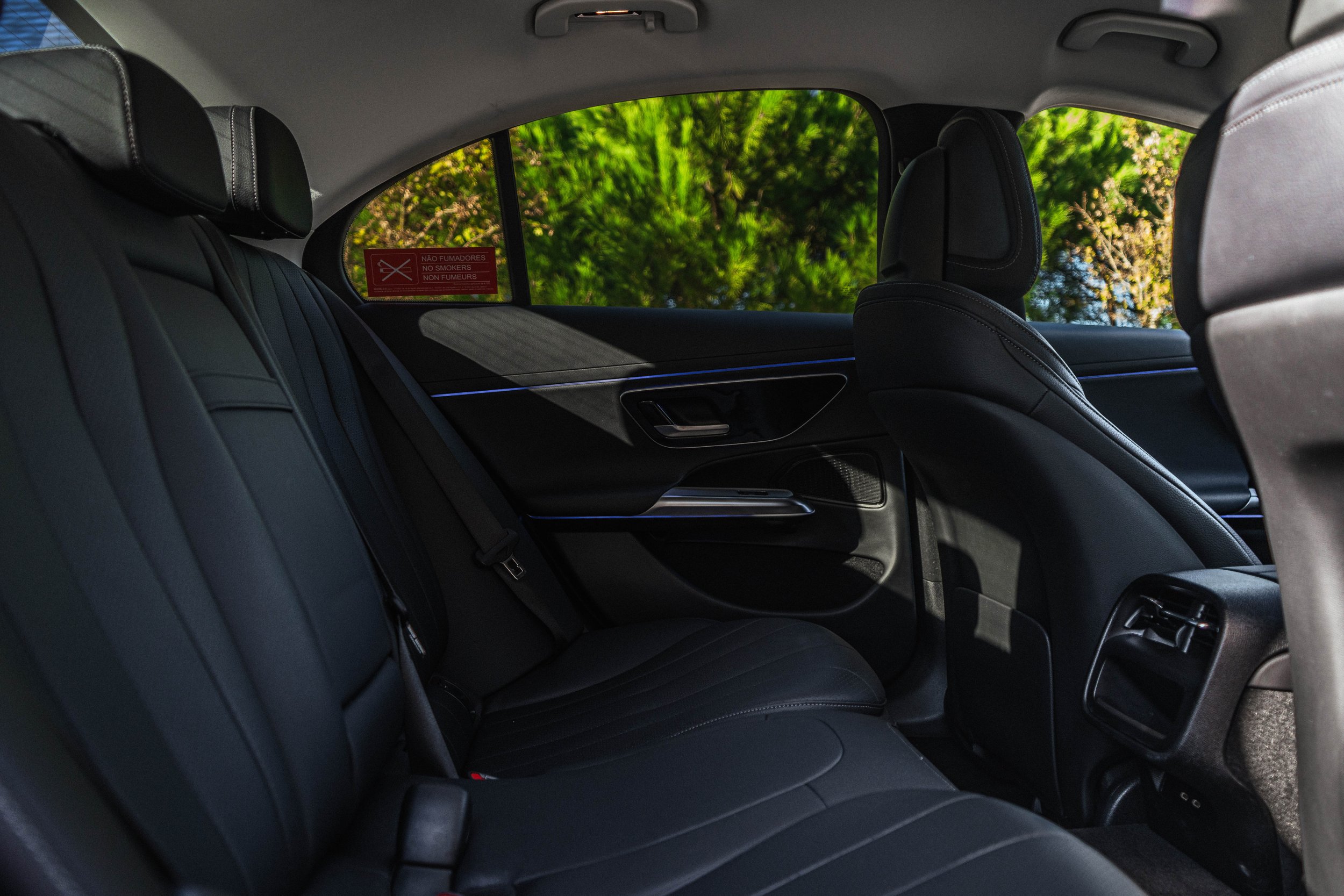 Interior de um carro com assentos de couro preto, janelas que mostram árvores verdes ao fundo