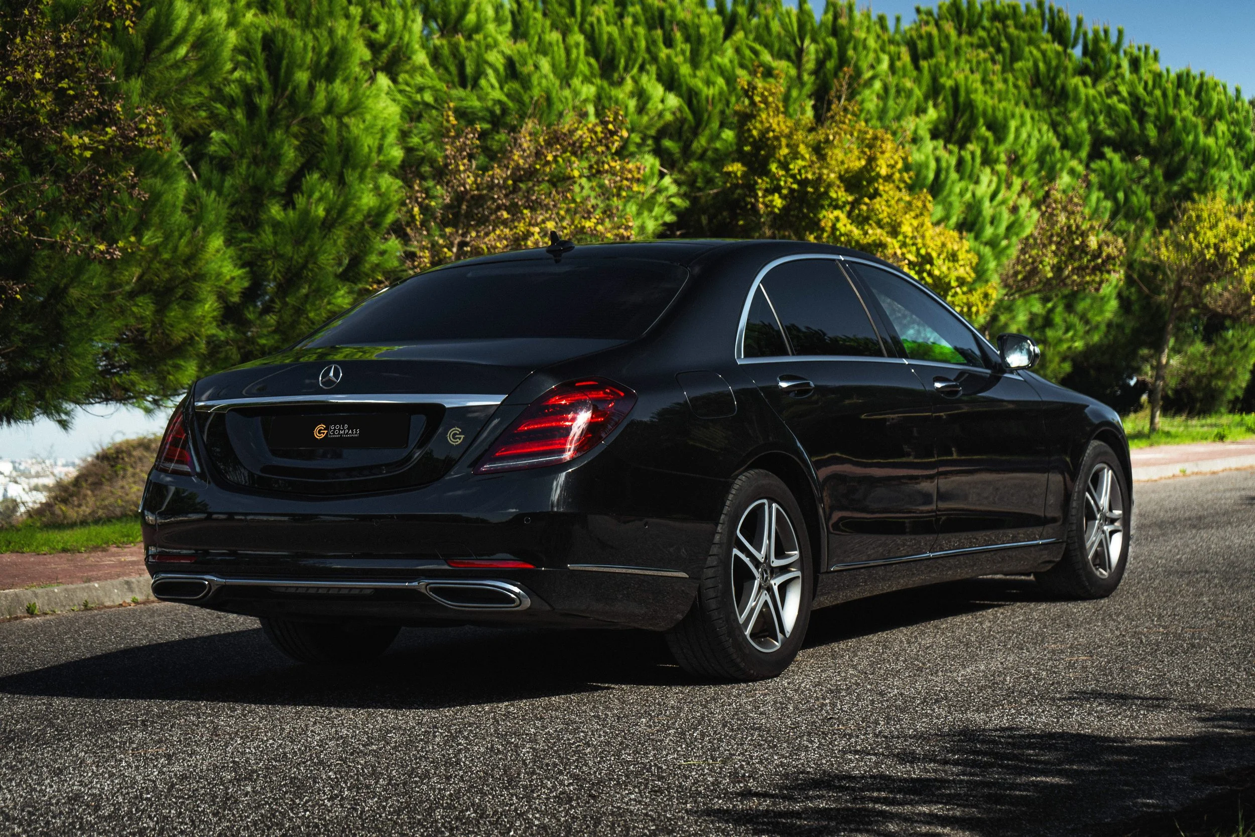Carro preto Mercedes-Benz estacionado na rua, com árvores verdes ao fundo.