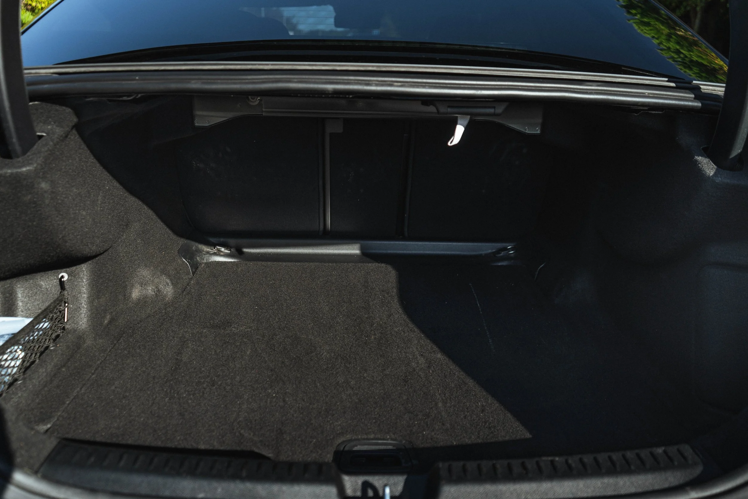 Revestimento do compartimento de bagagem de um carro vazio, com teto em couro preto e piso de carpete escuro.