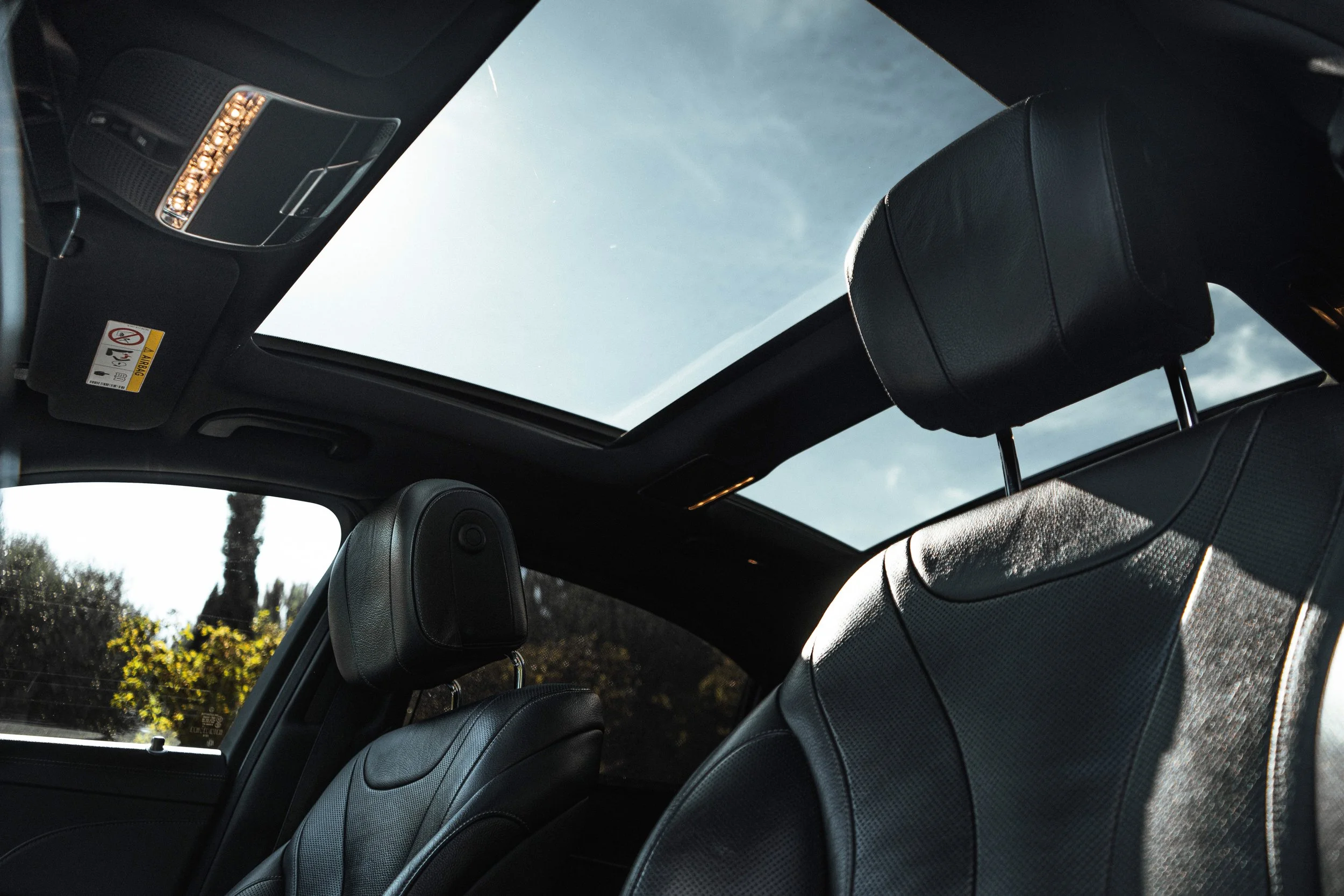 Interior de um carro com bancos de couro preto e teto de vidro panorâmico, mostrando o céu ao acima.