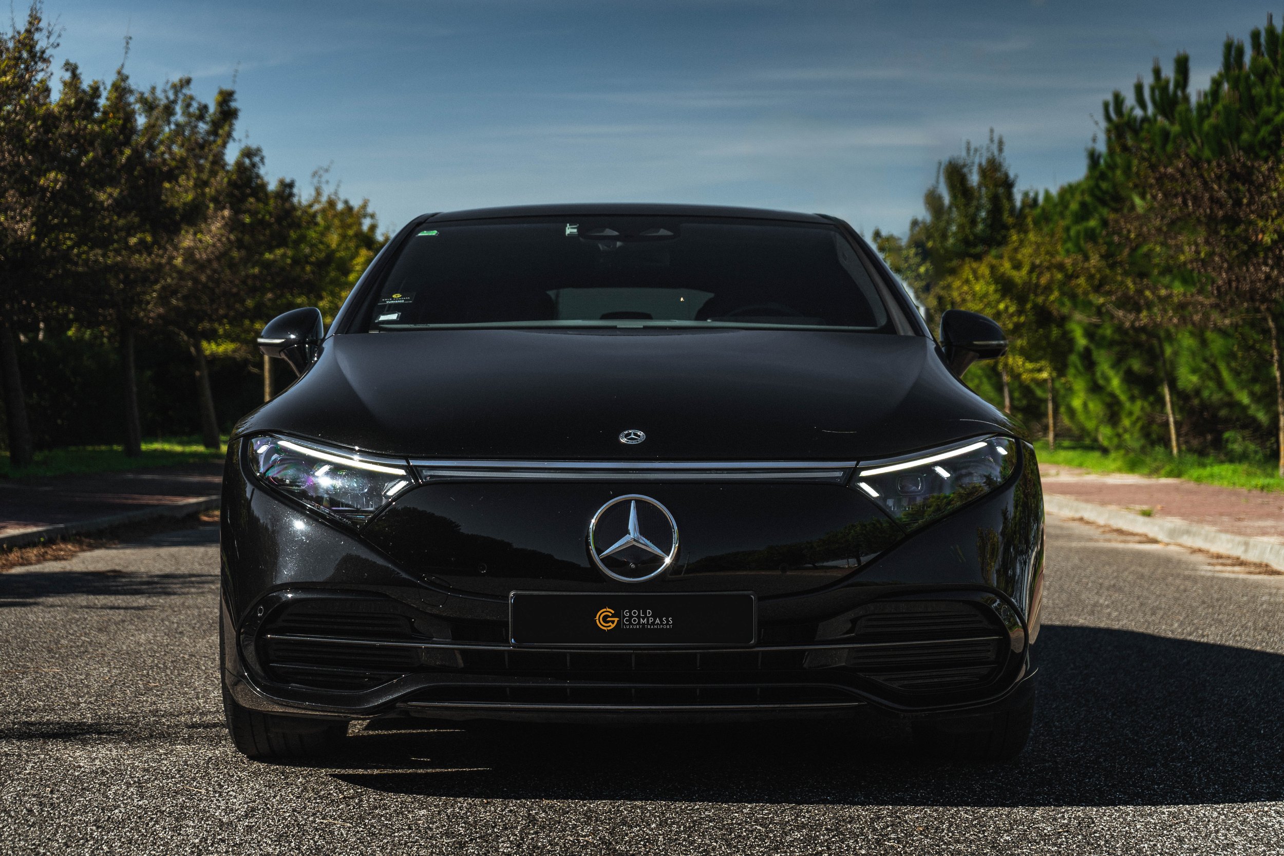 Carro preto Mercedes-Benz em frente na rua com árvores ao fundo.