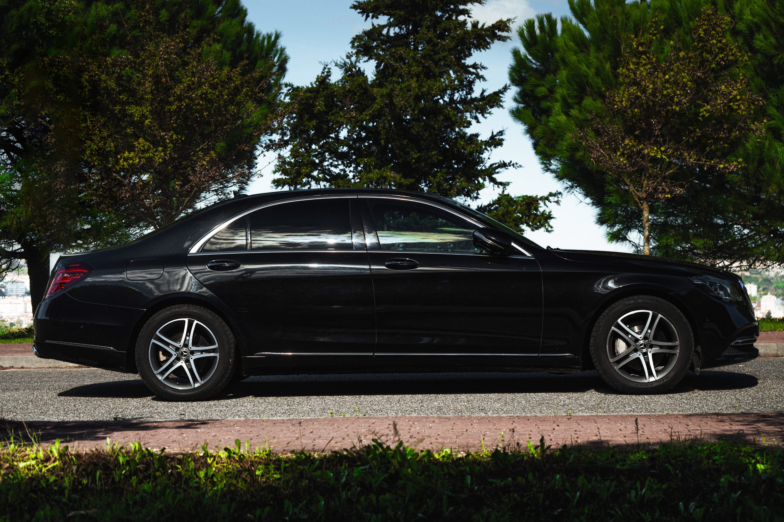 Carro preto estacionado na rua com árvores ao fundo e céu claro.