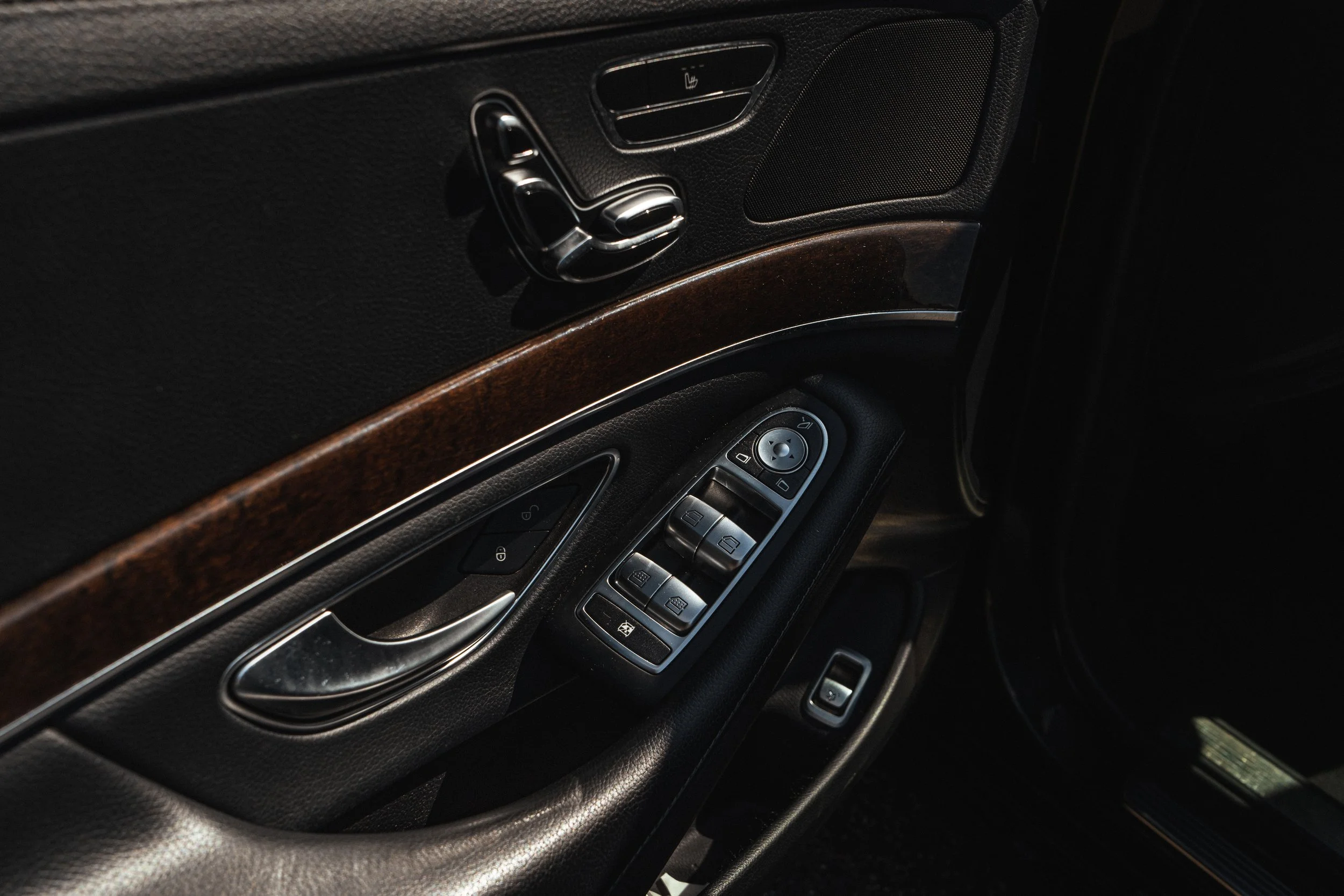 Painel de porta de carro com controles de janelas, espelhos e trava de portas, acabamento em madeira e tecido preto.