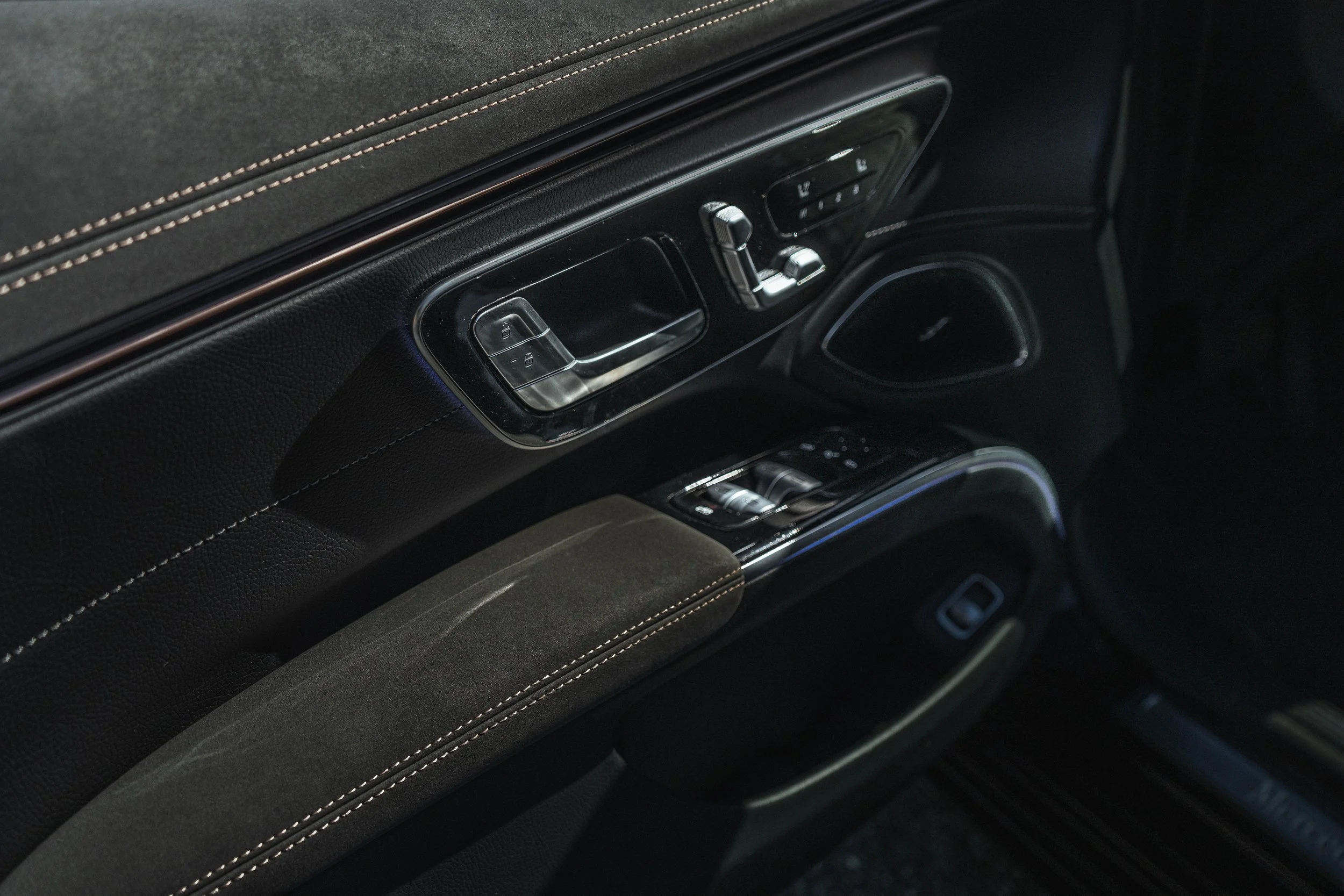 Tela aqui em cima e controles de janelas, espelhos e bancos na porta de um carro de luxo, com acabamento em couro preto e costura marrom.