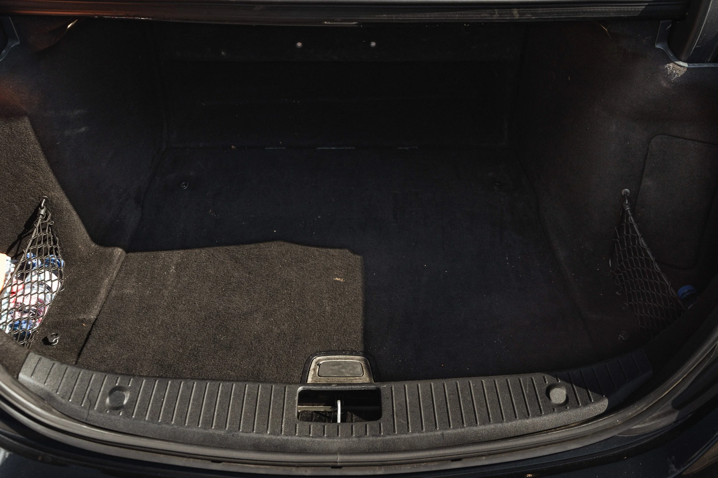 Maleta de carro vazia, com duas redes laterais para objetos, piso de carpete preto e uma área de armazenamento lateral.