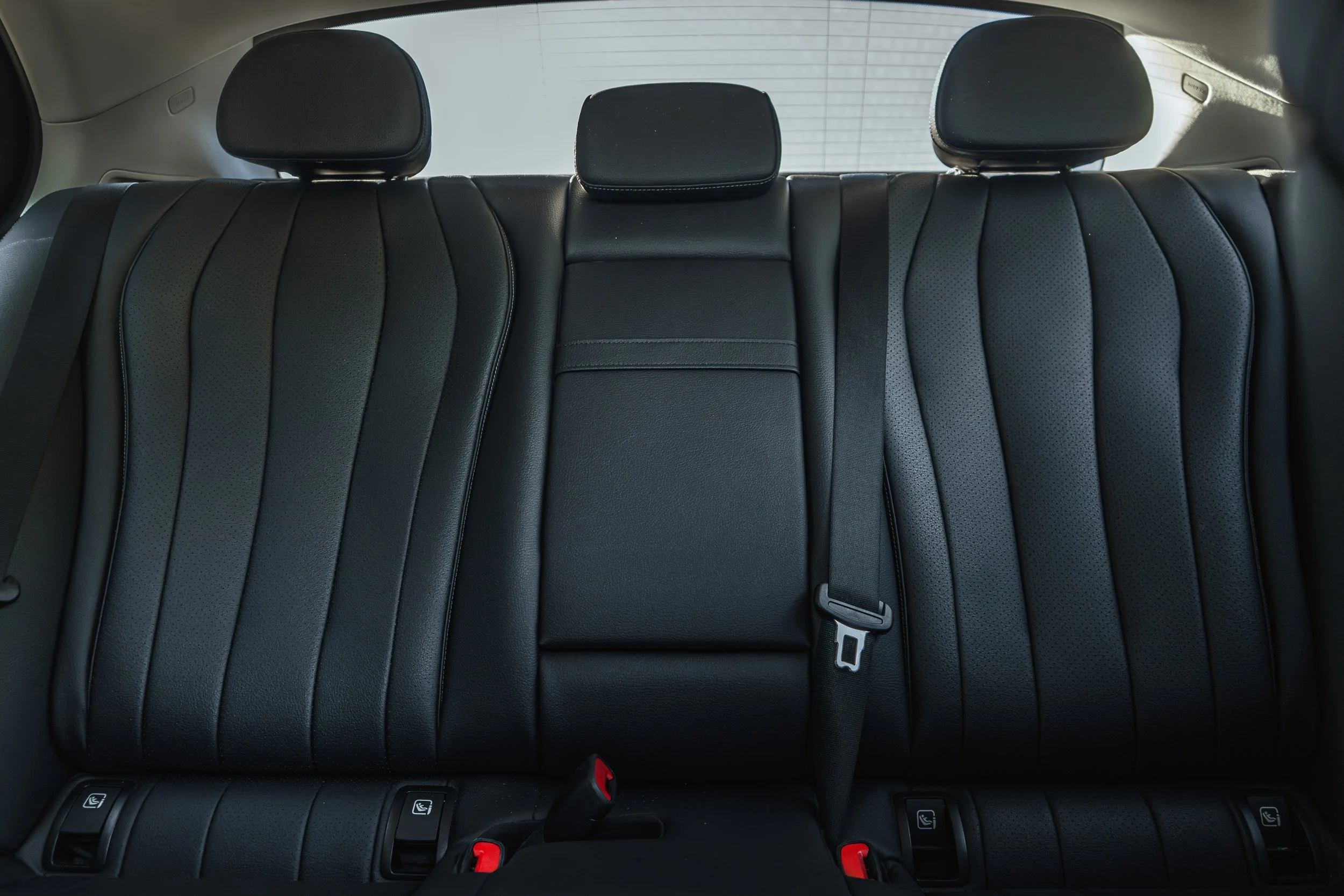 Assento traseiro de carro em couro preto com três cabeceiras ajustáveis e cintos de segurança.
