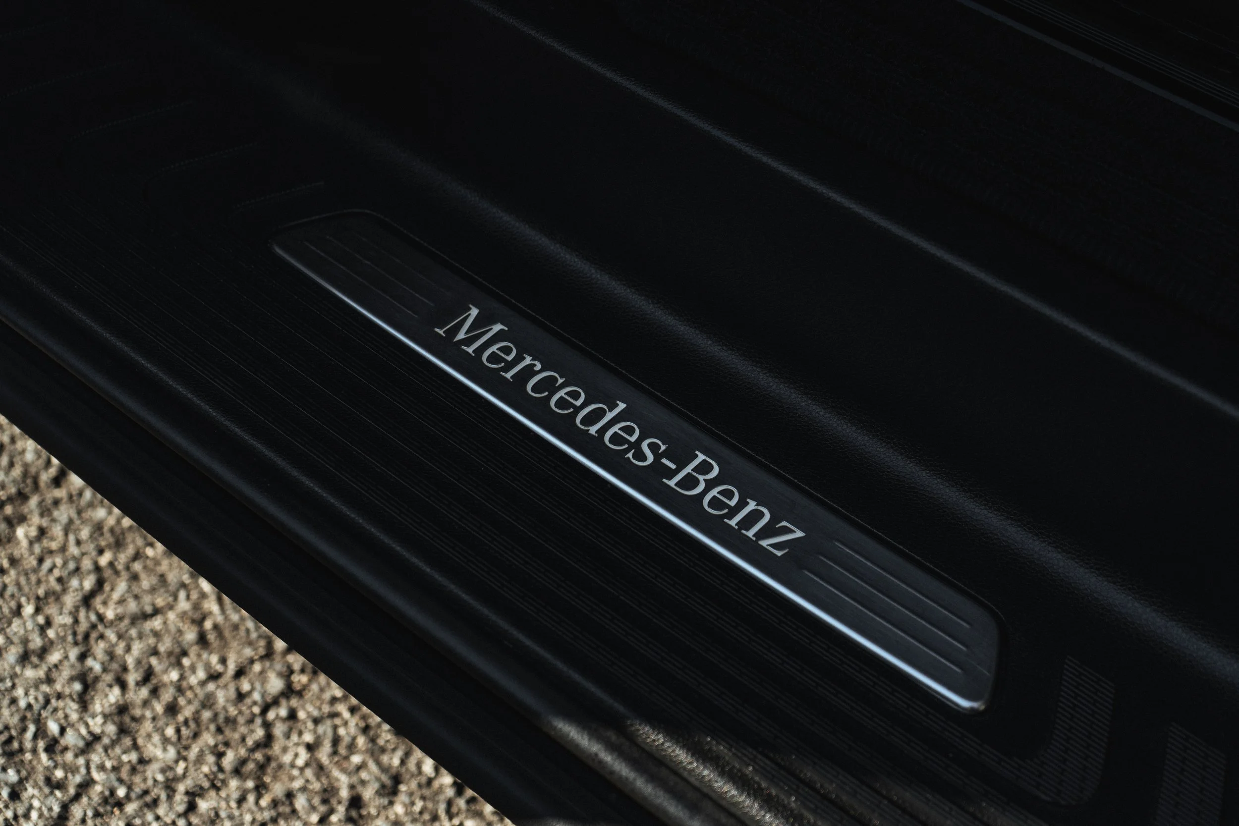 Imagem do degrau de uma porta de carro Mercedes-Benz, com o logotipo da marca em destaque, feito de material preto com detalhes em metal.