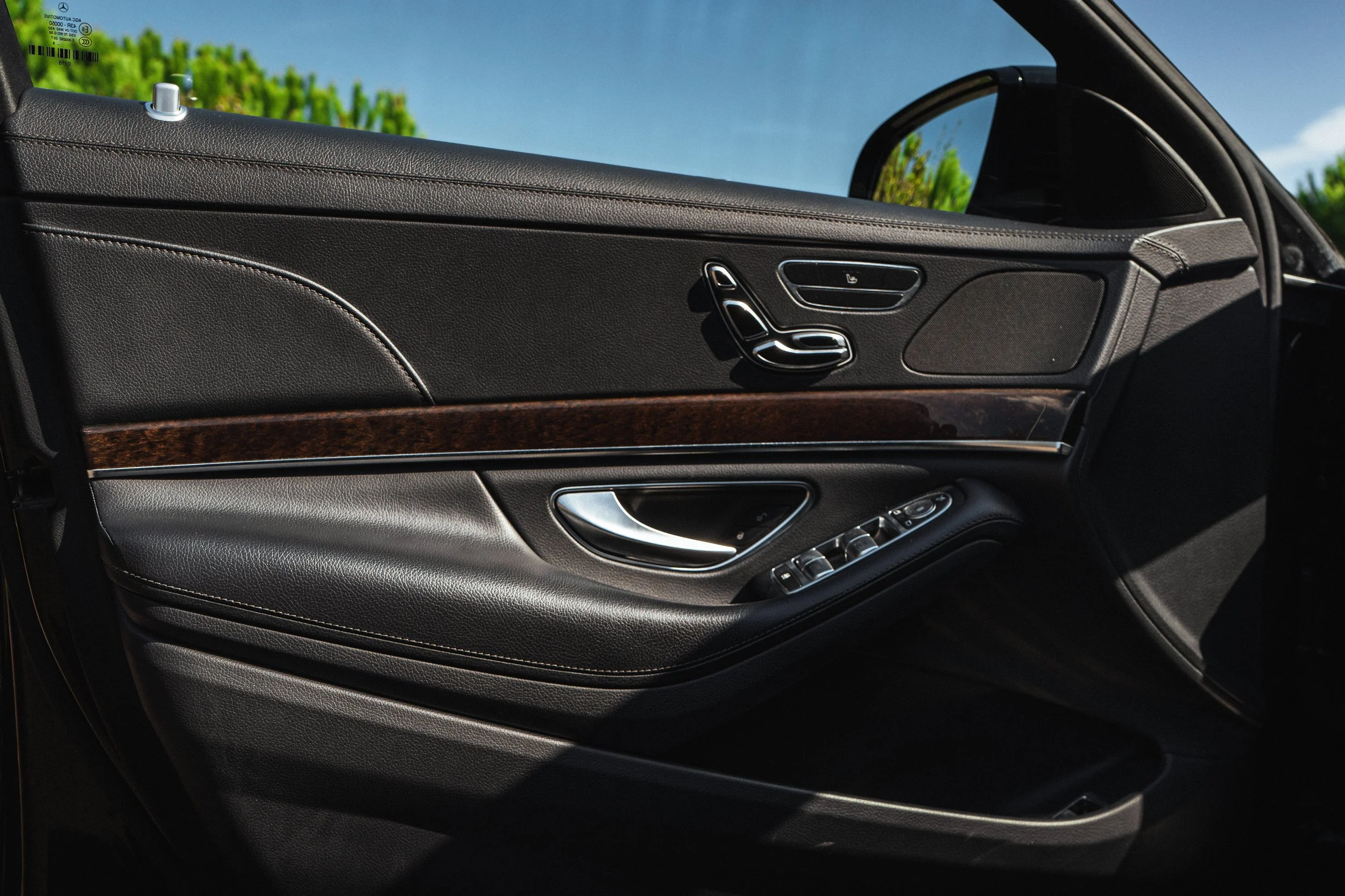 Interior de carro, painel de porta com comandos de ajuste de assento, controle de volume, e alavanca de porta em acabamento de couro e madeira