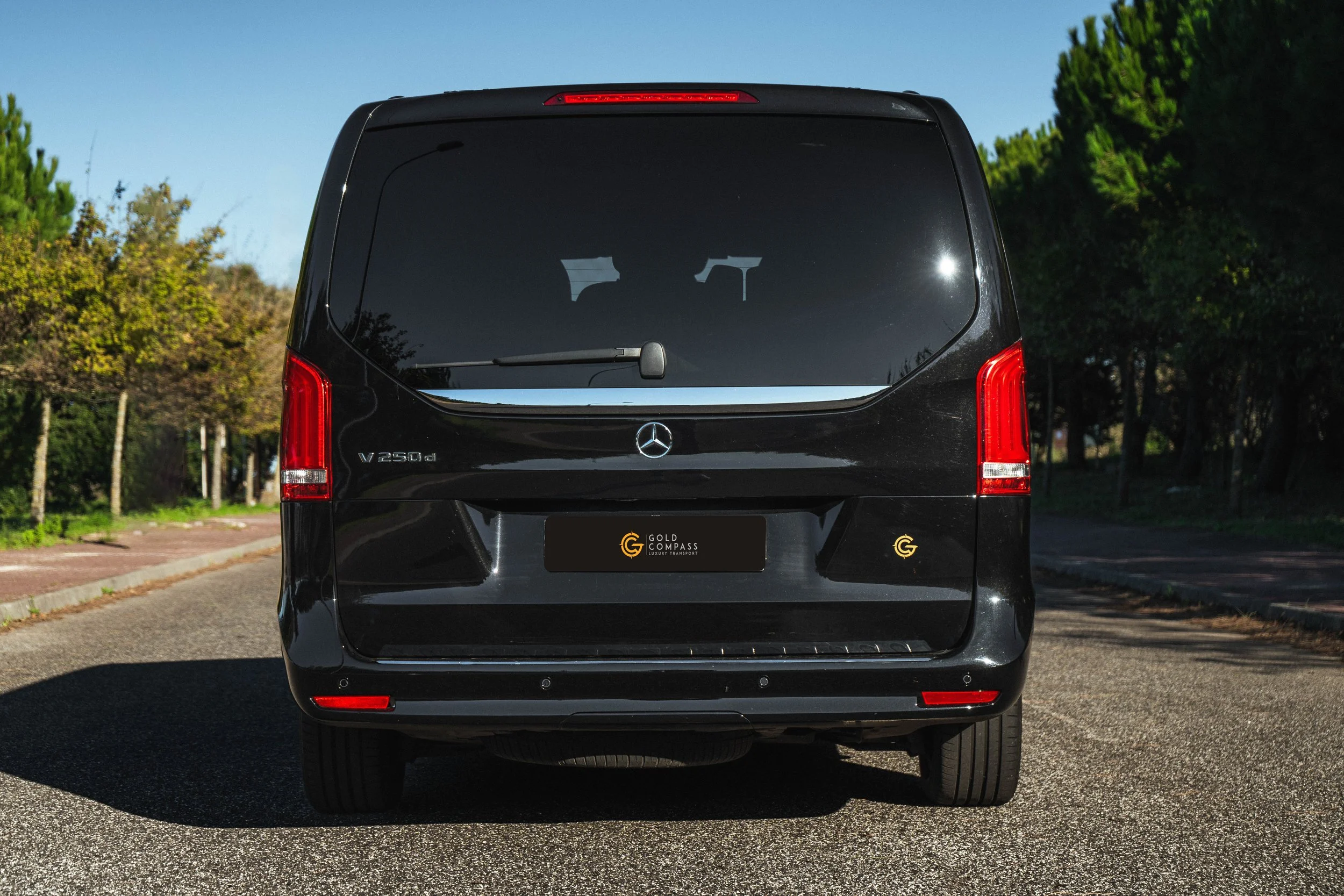 Furgão preto Mercedes-Benz V250d estacionado na rua com árvores ao fundo.
