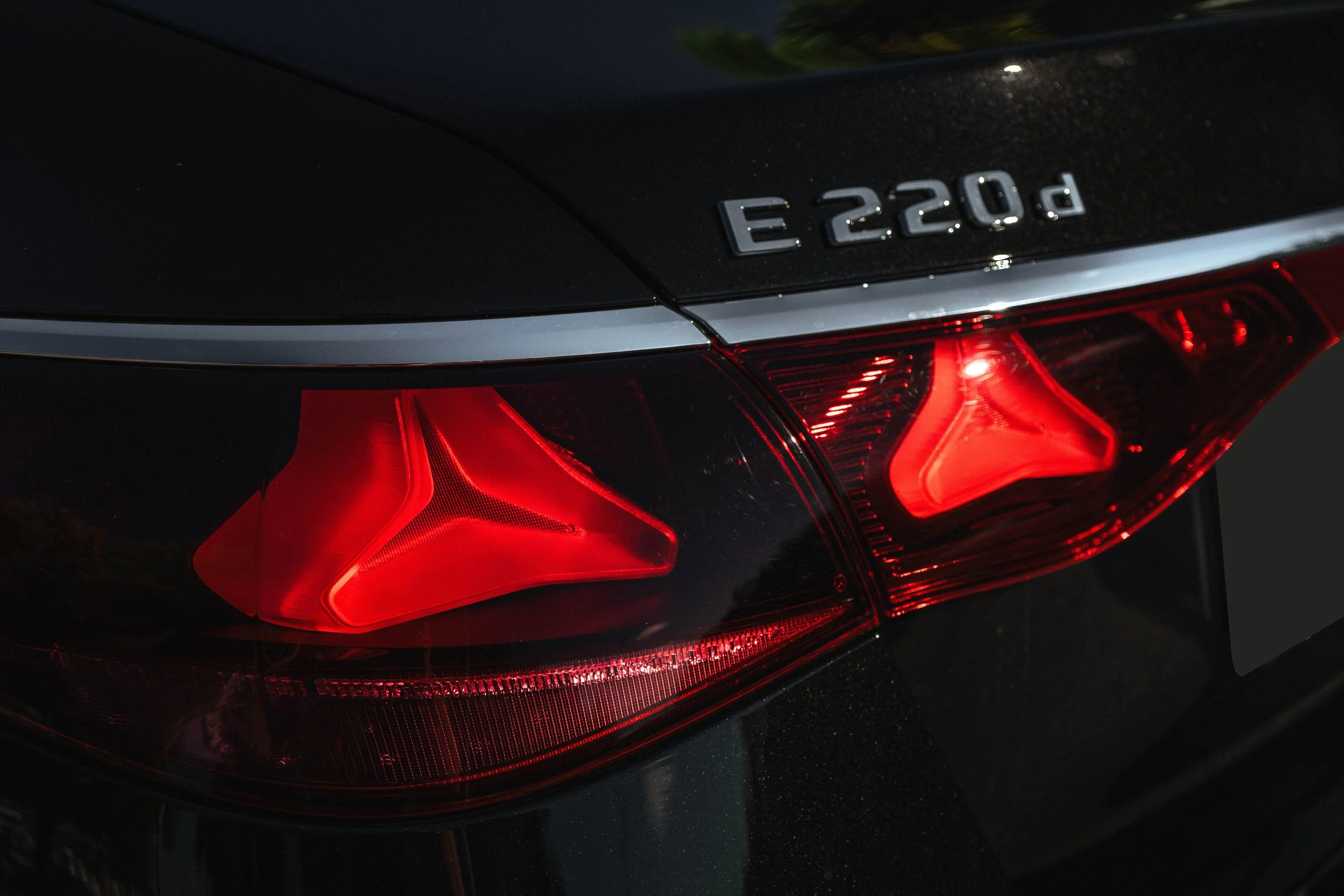 Foco de lanterna traseira de carro preto, com a marcação E 220d na parte superior.