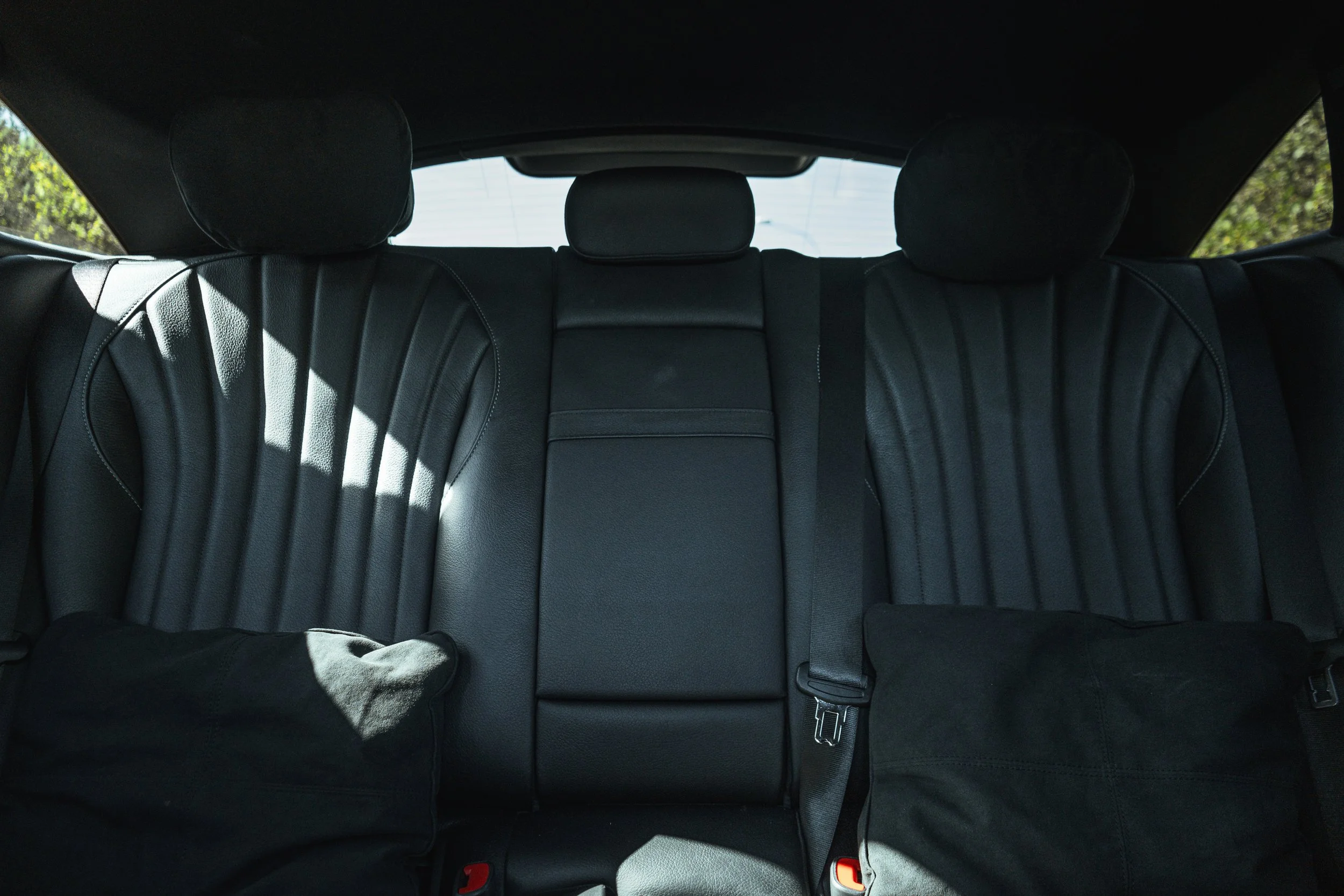 Assentos traseiros de um carro de couro preto com cintos de segurança, refletindo luz natural.