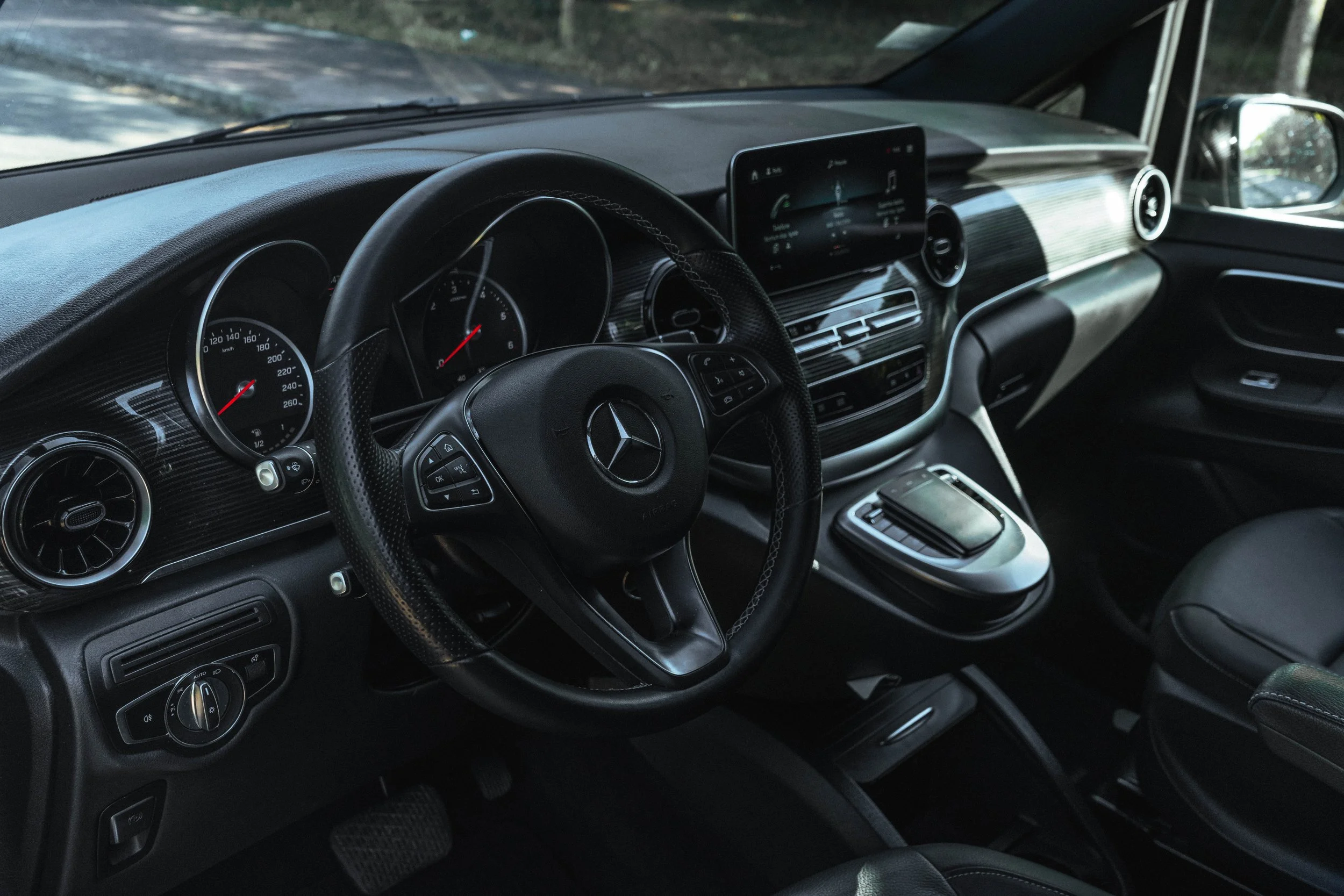 Interior de carro Mercedes-Benz com painel digital, volante com comandos, tela de infotainment, sistema de ar-condicionado e câmbio no centro.
