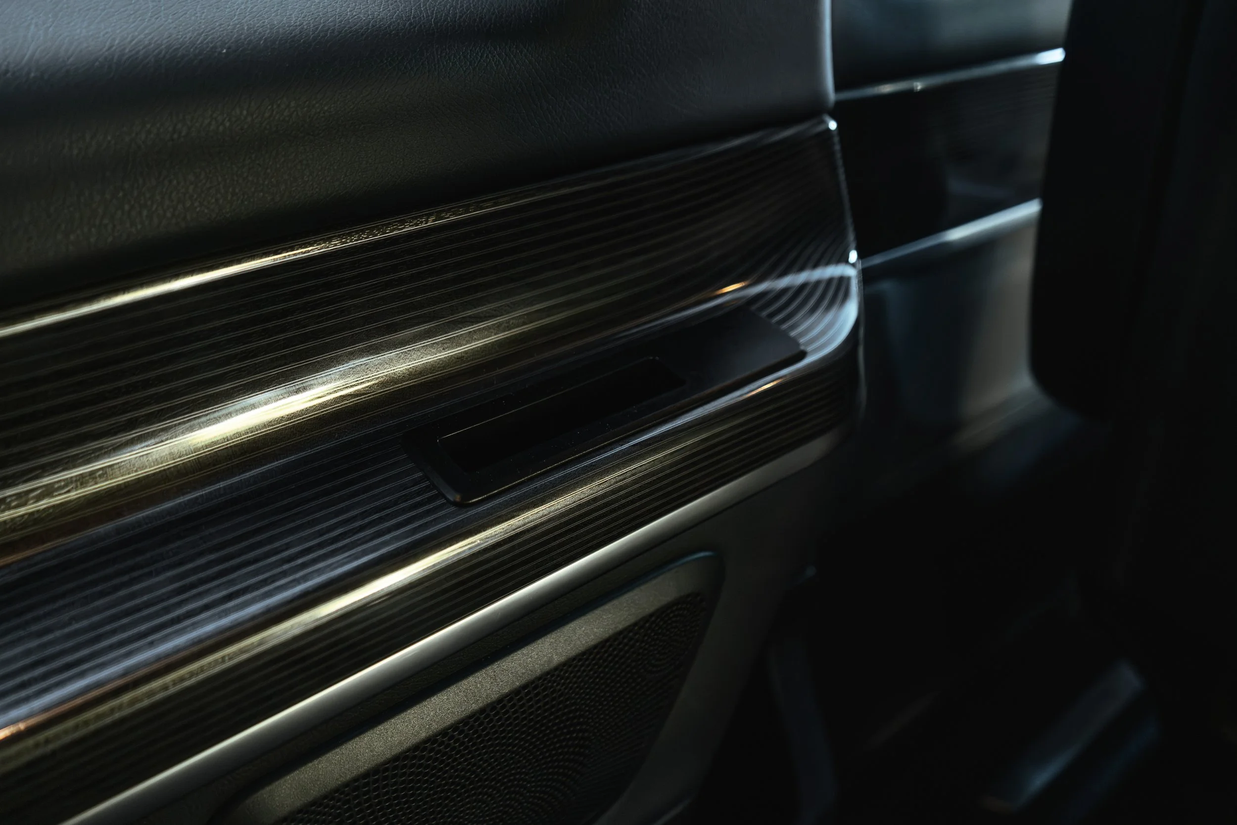 Detalhe do interior de um carro, mostrando painel lateral com acabamento em detalhes em linha e uma pequena gaveta metálica.