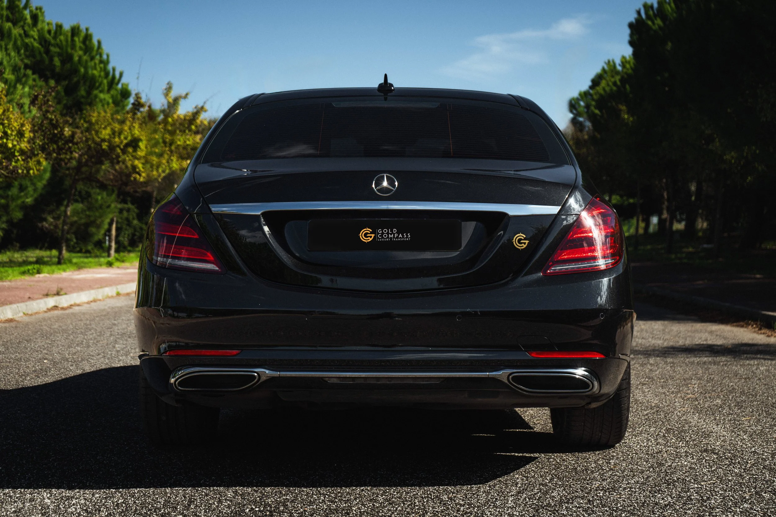 Fundo de carro Mercedes-Benz preto estacionado na rua com árvores verdes ao fundo.