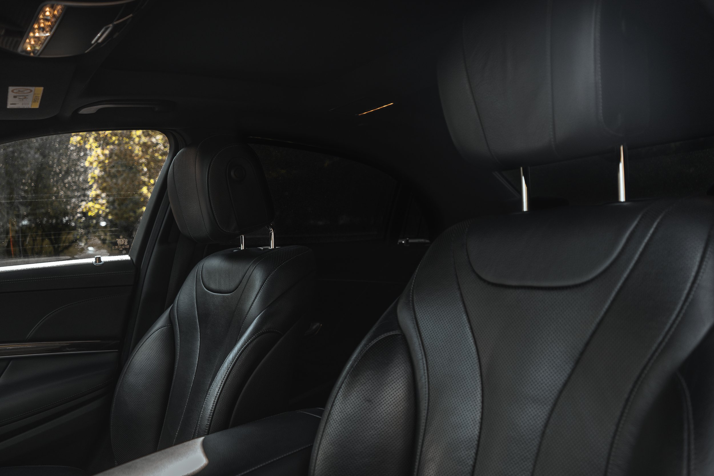 Interior de carro com assentos de couro preto e janelas pequenas, com árvores visíveis do lado de fora.