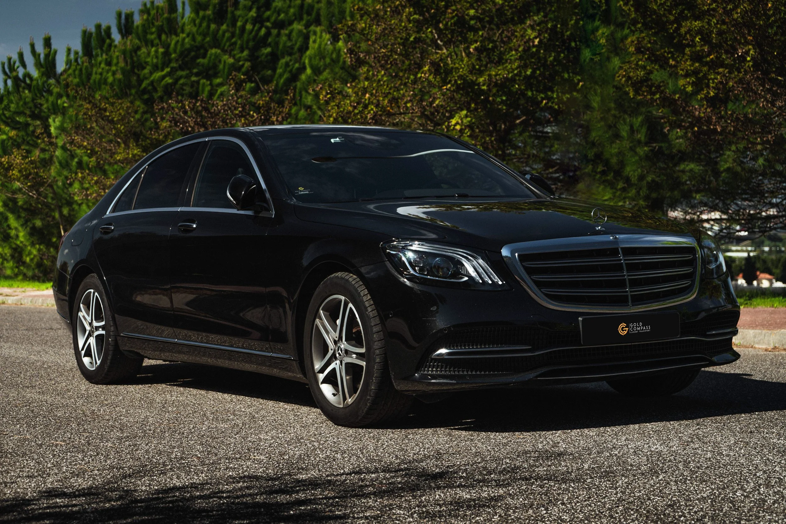 Carro preto de luxo, modelo sedã, estacionado na rua com árvores verdes ao fundo.