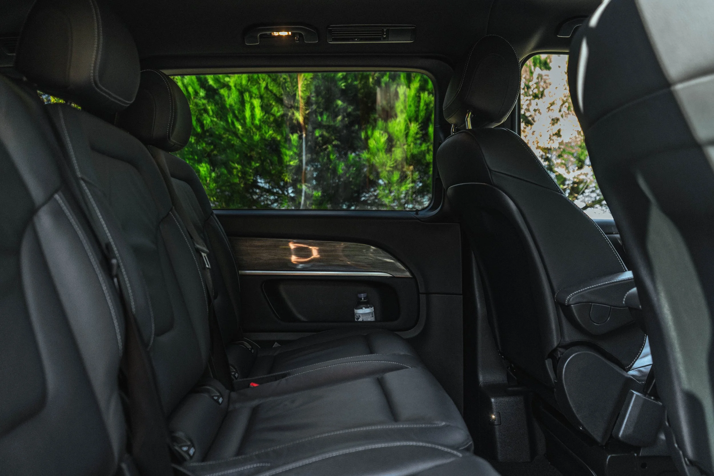 Interior de carro com assentos pretos, janela com vista para árvores verdes.