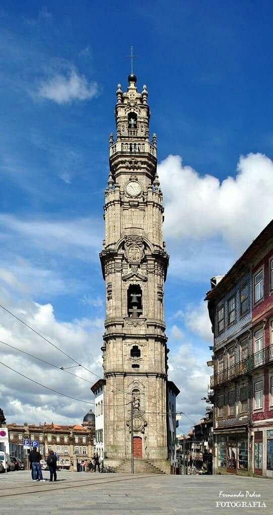 Torre de relógio antiga em uma praça urbana, com prédios ao redor e pessoas caminhando