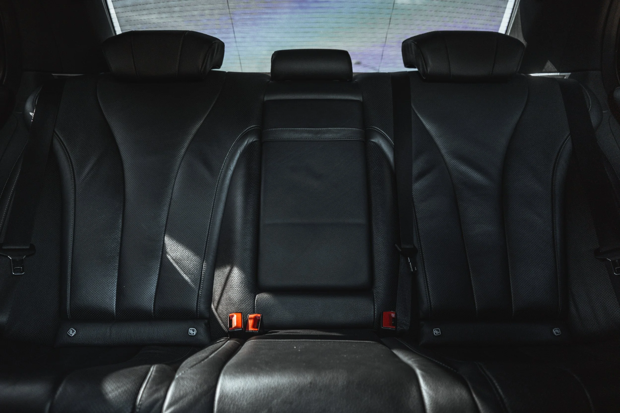 Assentos traseiros de carro em couro preto com apoios de cabeça e cintos de segurança.