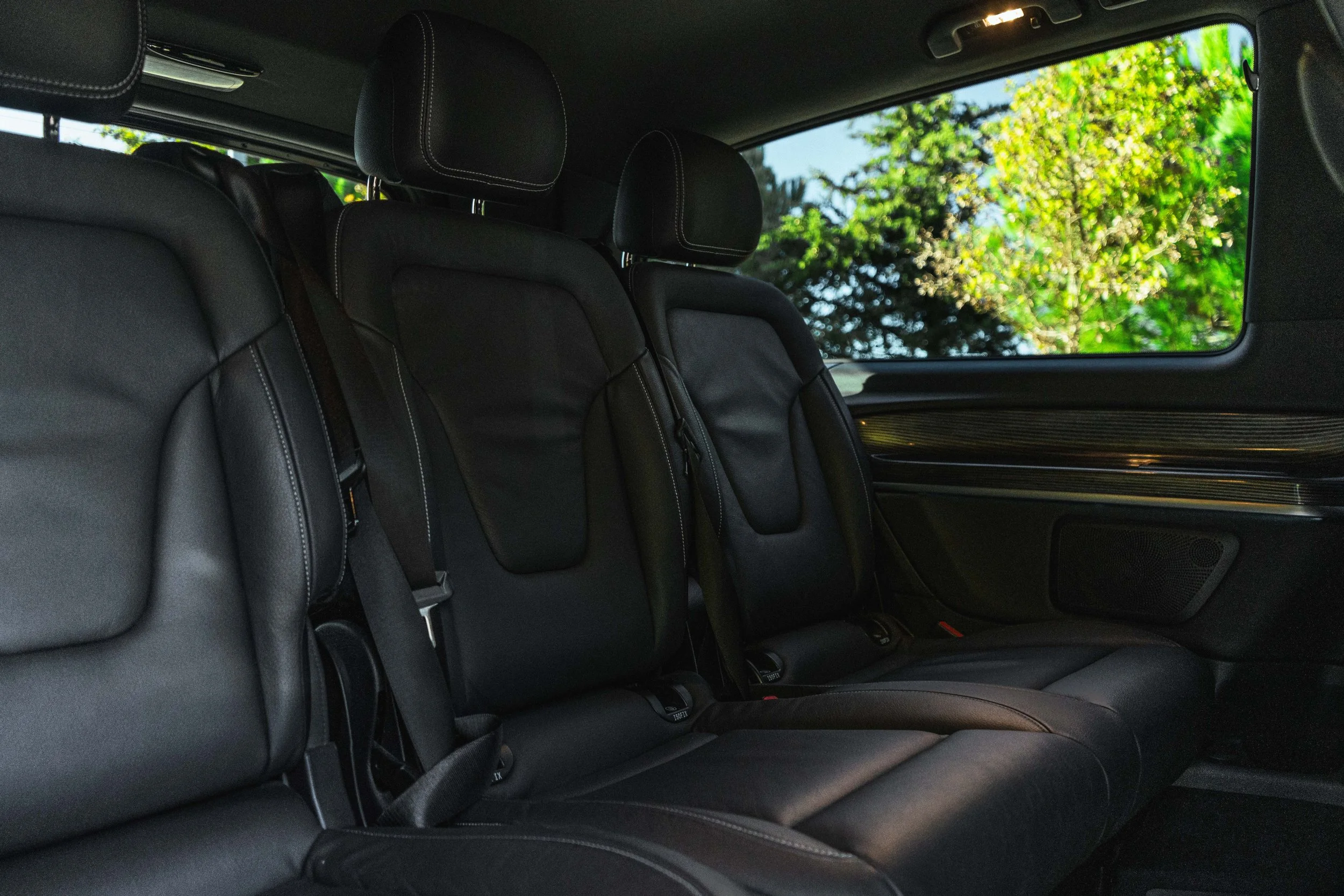 Assentos de couro preto no interior de um carro, com vista para uma janela com árvores verdes ao fundo.