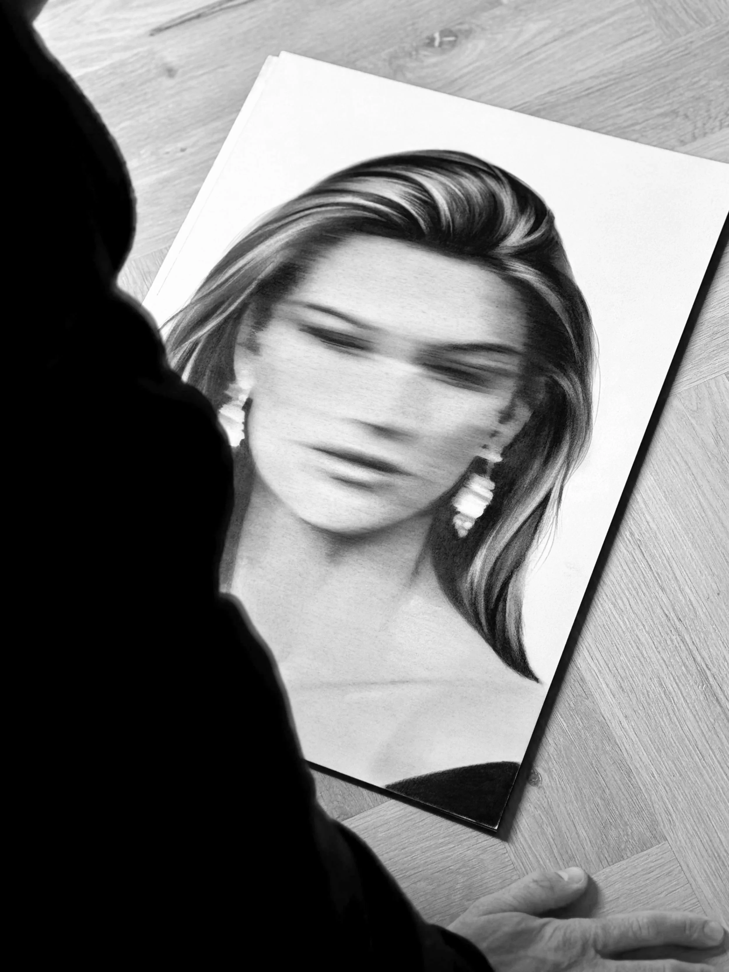 Black and white photograph of a hair portrait drawing on paper, placed on a wooden floor, with a person in the foreground.