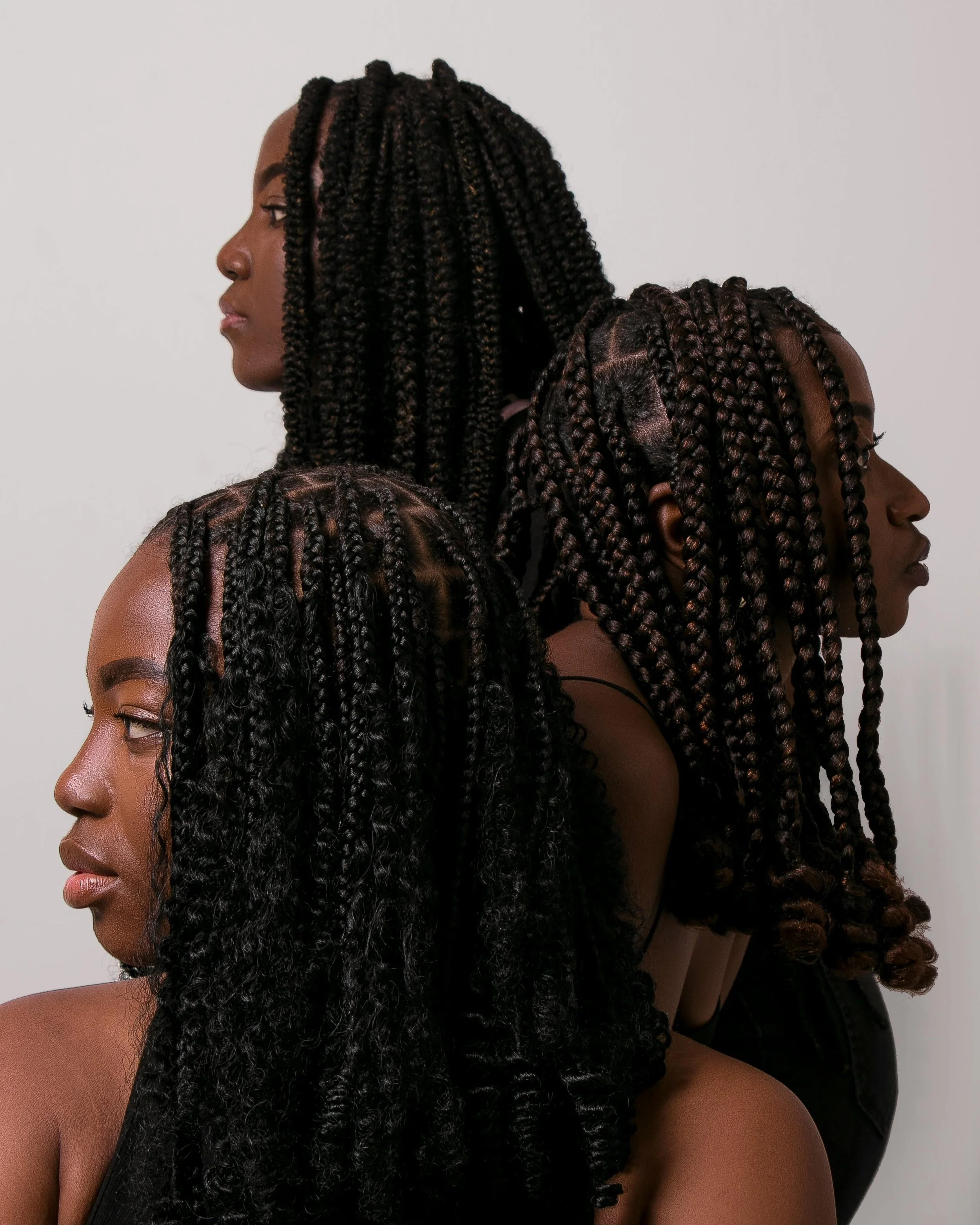Four women with braided hairstyles standing in profile against a plain background.