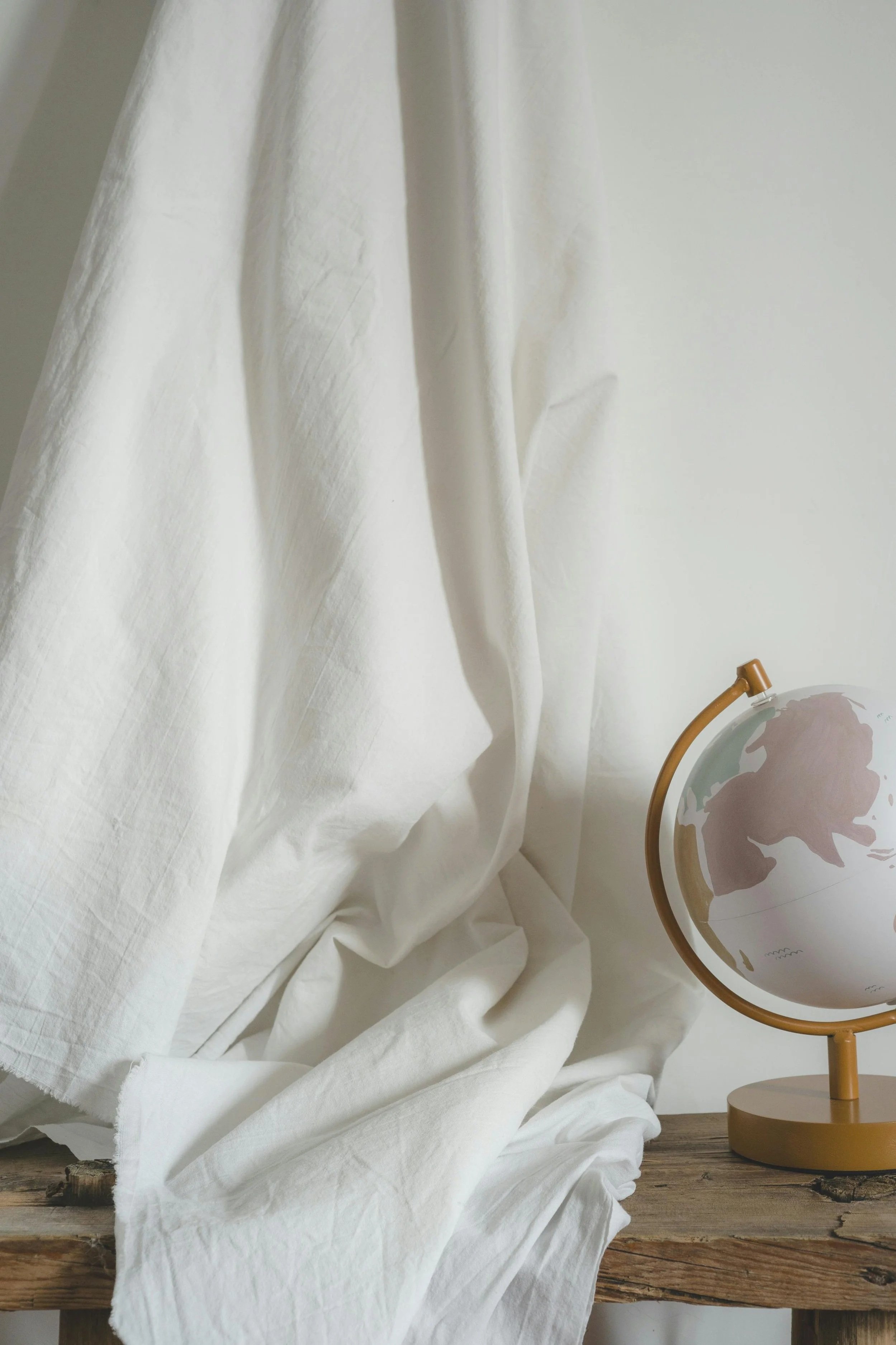 A white curtain draped over a rustic wooden surface with a globe-shaped decorative item on a stand to the right.
