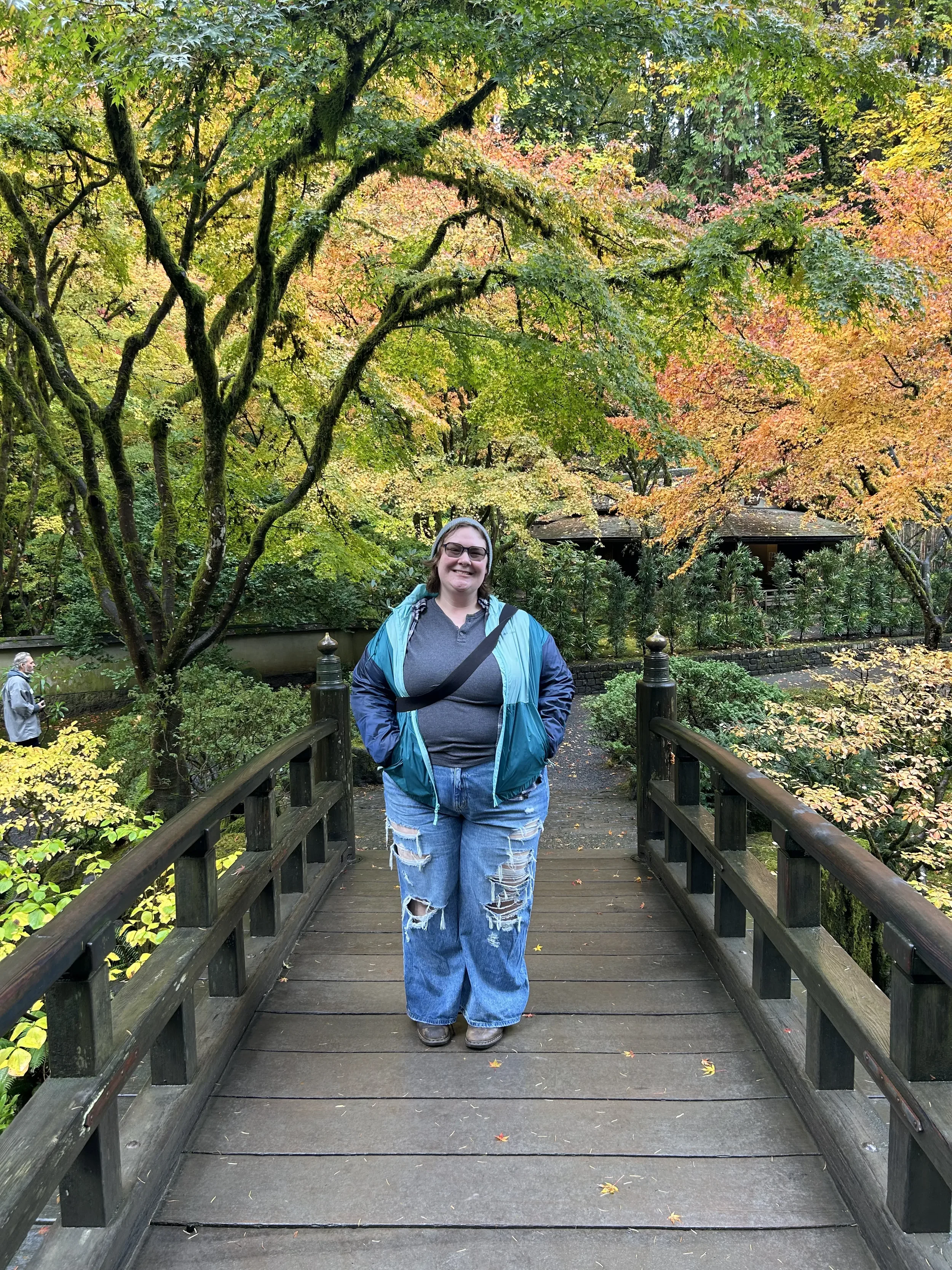 A woman standing on a wooden bridge in a park with colorful autumn trees in the background.